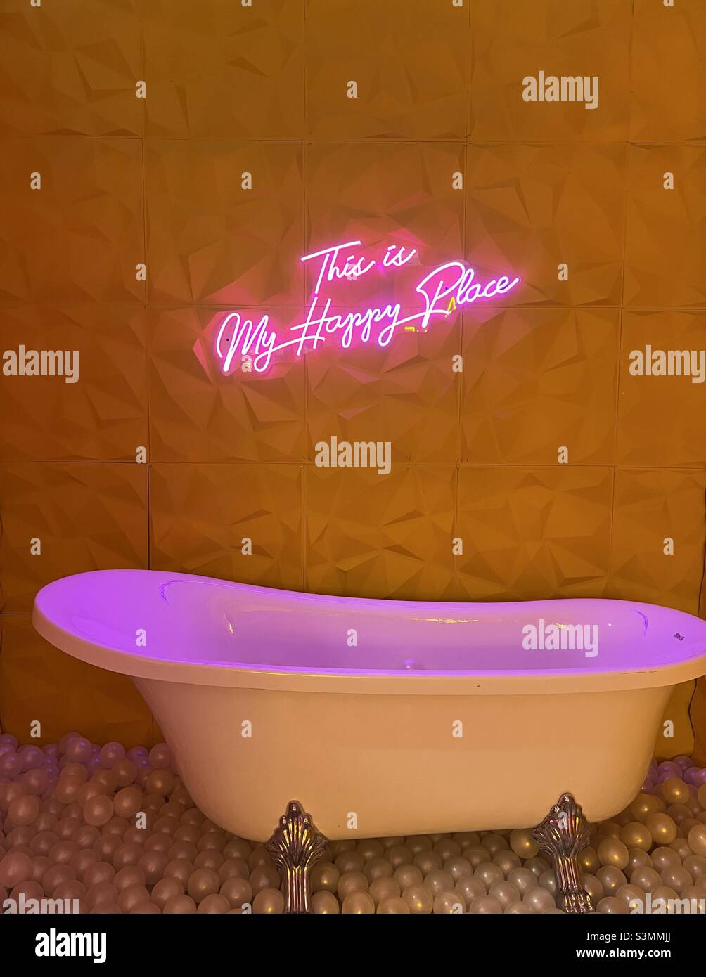 Rosa und gelbe Badewanne mit Neonschild, dies ist mein glücklicher Ort Stockfoto