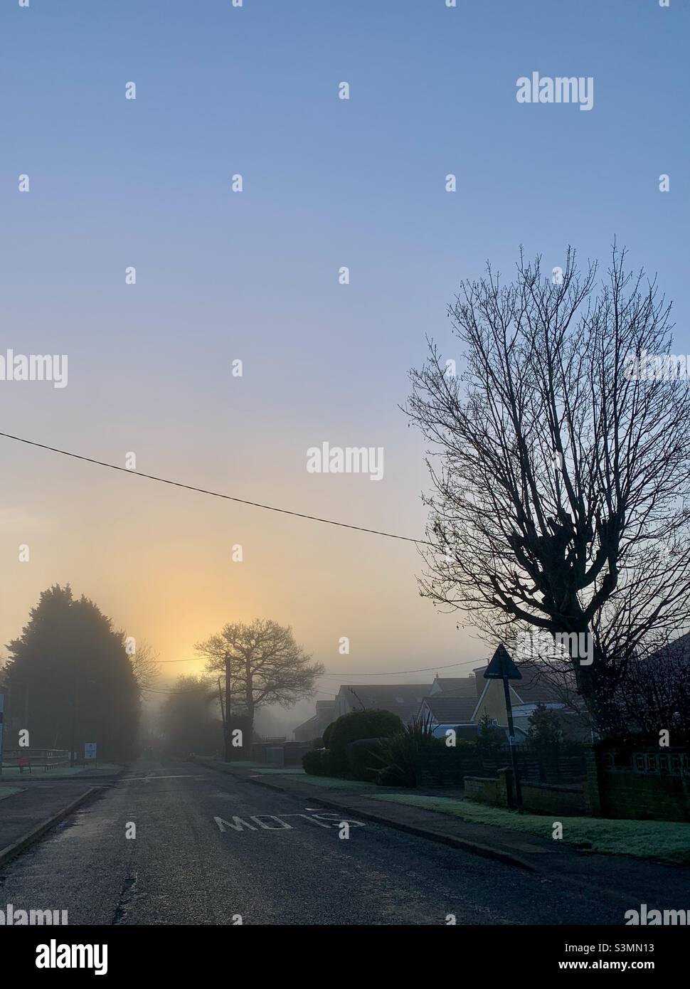 Sonnenaufgang und ein nebliger Start in den Tag in Oxfordshire. Am frühen Morgen. Eine leere Straße, die sich in Richtung Sonnenaufgang schlängelt. Stockfoto