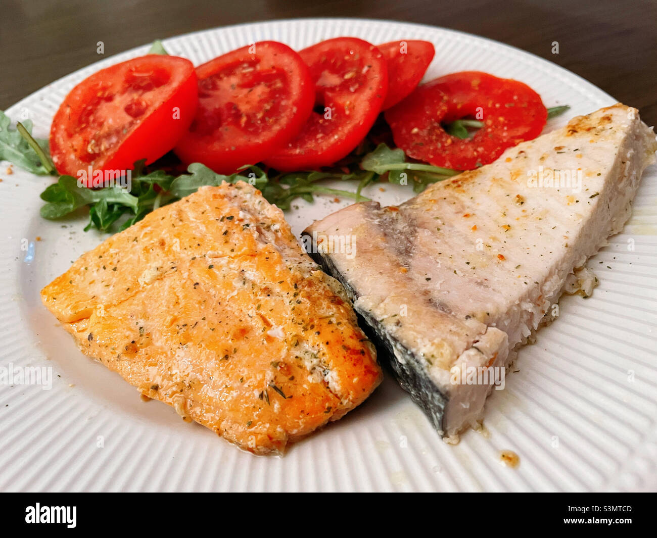 Nahaufnahme eines Gourmet-Vorspeisen aus gebratenem Lachs und Schwertfisch mit einem gesunden Tomatensalat Stockfoto