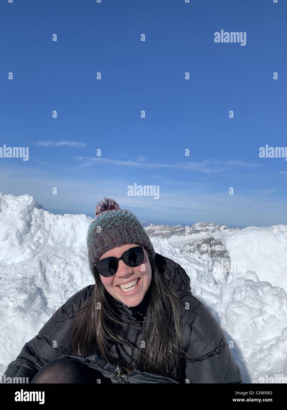 Lächelnde Frau sitzt auf einem schneebedeckten Berg in Engelberg, Schweiz. Winterurlaub Genuss. Stockfoto