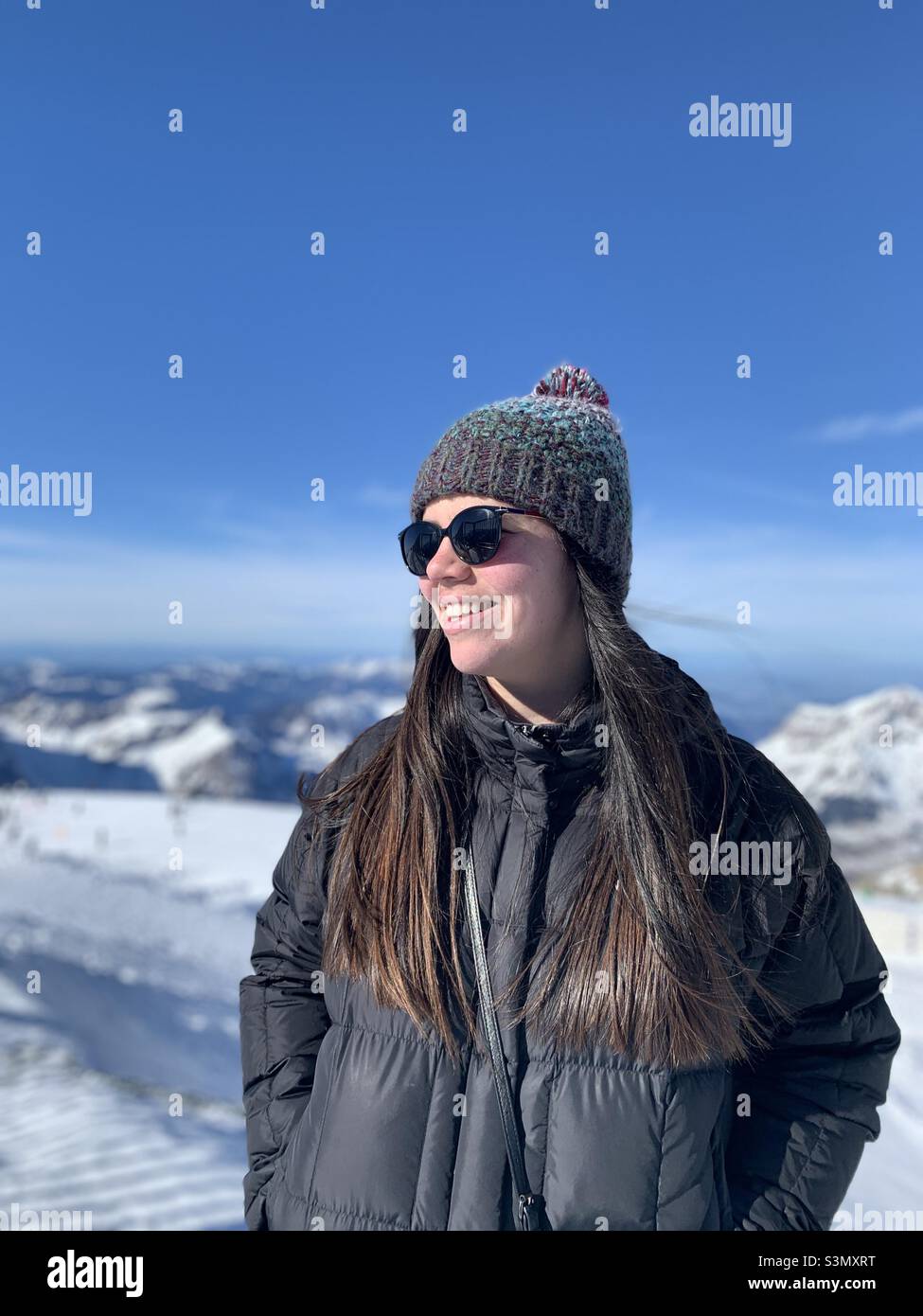 Die junge Frau schaut lächelnd in den Winterferien auf den schneebedeckten Berg in den Uri Alpen, Engelberg, Schweiz Stockfoto