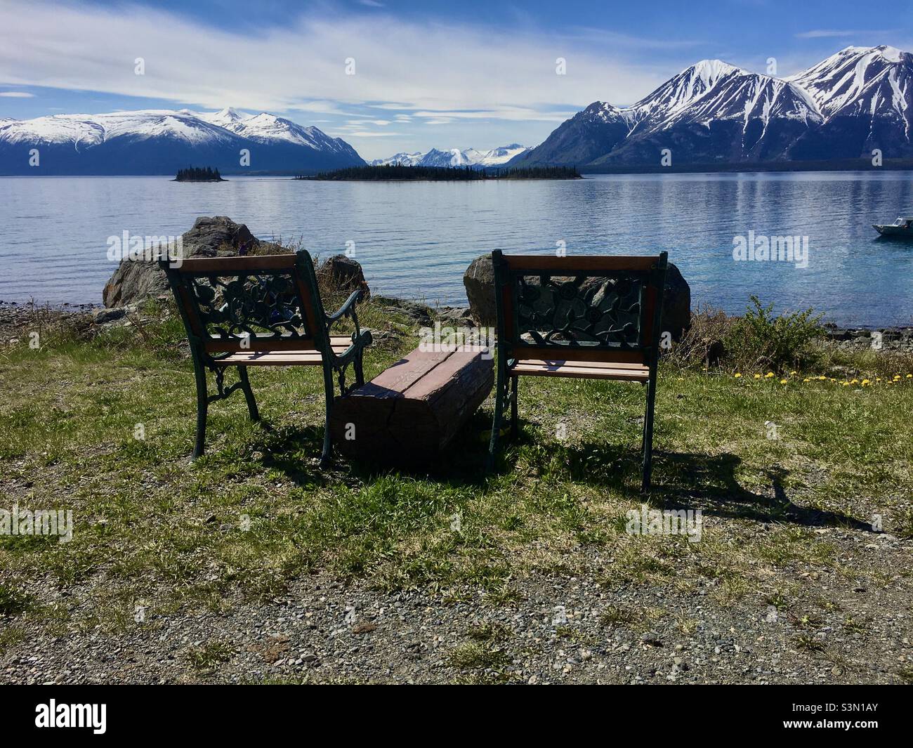 Ruhige Szenerie mit Blick auf den Atlin Lake in British Columbia, mit schneebedeckten Bergen und Inseln im Hintergrund. - Smartphone-aufgenommenes Stockfoto