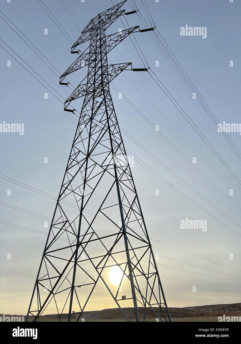 Ein hoch aufragender Strommast, der gegen die Morgensonne silhouettiert wurde. In Der Nähe Von Calgary, Alberta, Kanada. Stockfoto