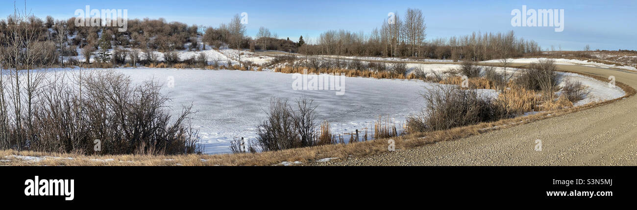 Panorama einer Straße um einen Teich, der zu schmelzen beginnt. In den Ausläufern, in der Nähe von Calgary, Alberta, Kanada. Stockfoto