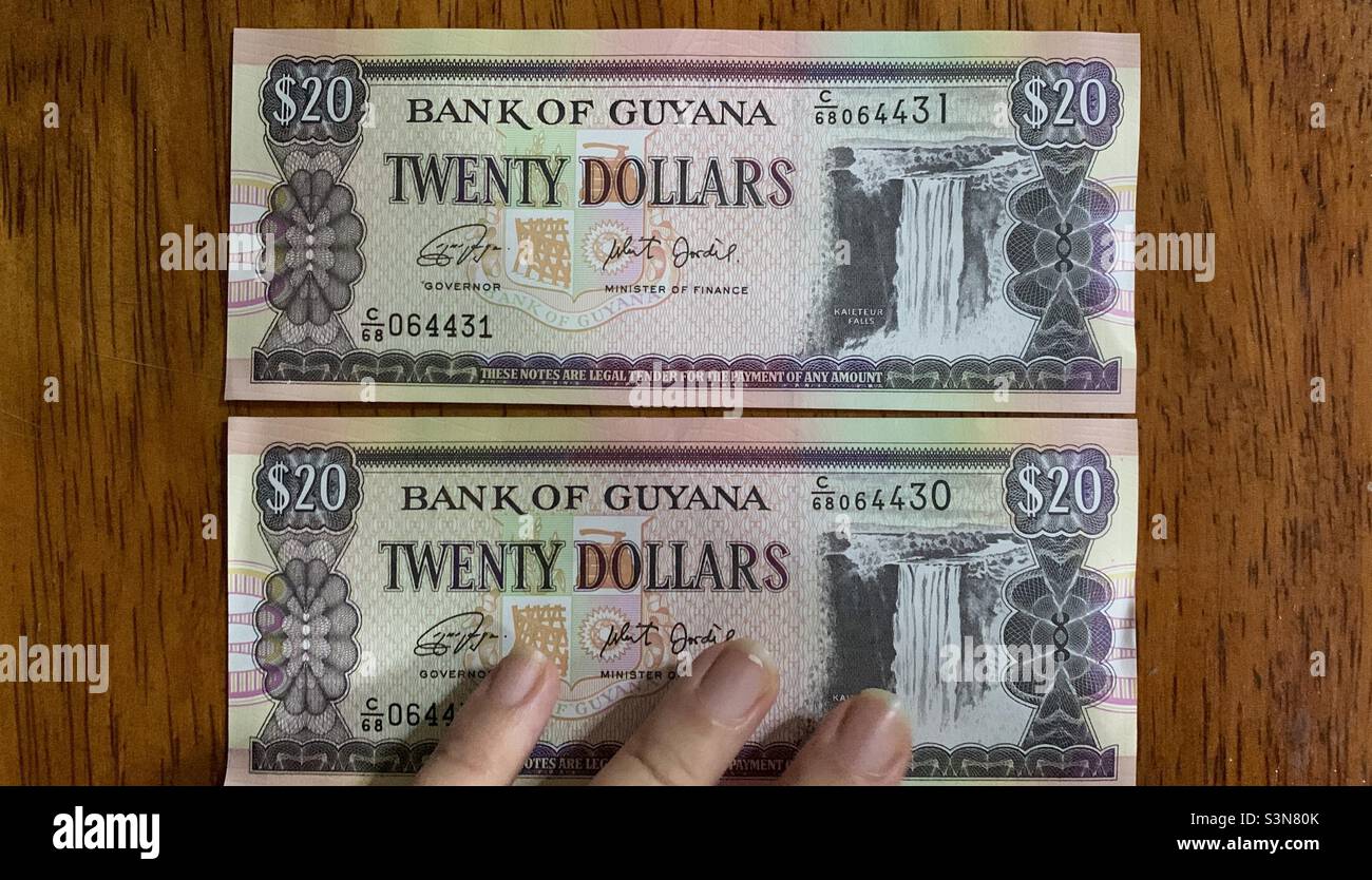 Hand auf zwei zwanzig-guyanischen Dollar-Scheine. Kubaner in Guyana. Georgetown, Guyana. Stockfoto