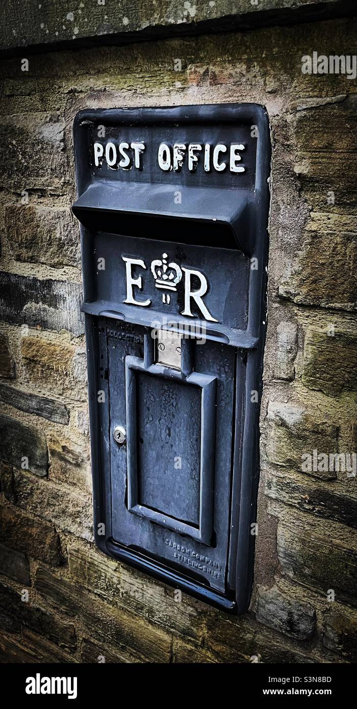 ‘Return to Sender’ ein seltener schwarzer Briefkasten sitzt perfekt in einer Steinmauer in einem malerischen ländlichen Dorf Stockfoto