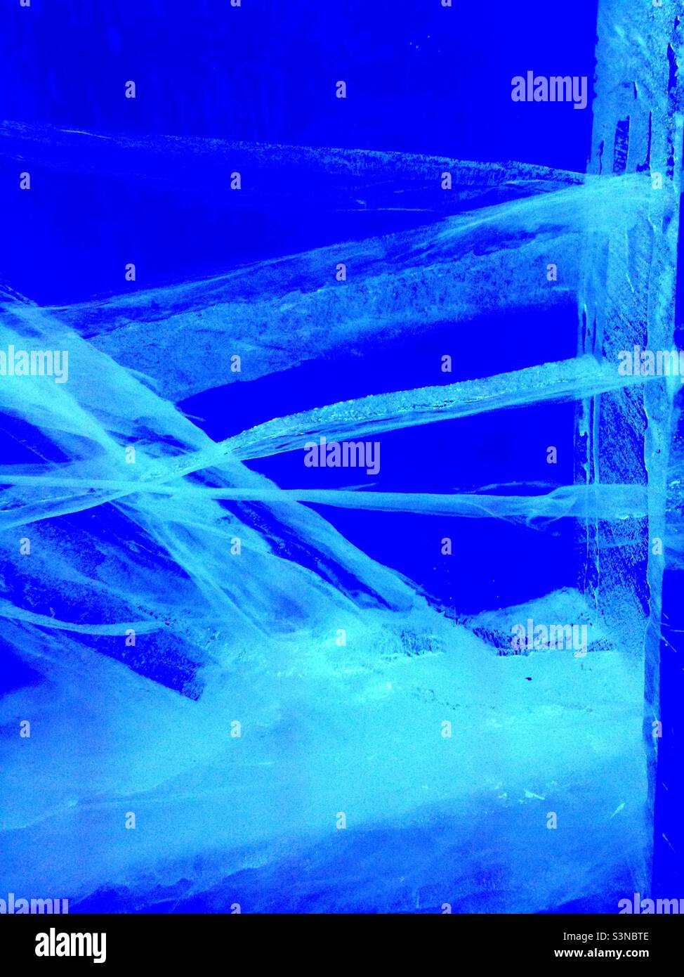 Nahaufnahme von Eis mit Rissen vor blauem Hintergrund. - Smartphone-aufgenommenes Stockfoto