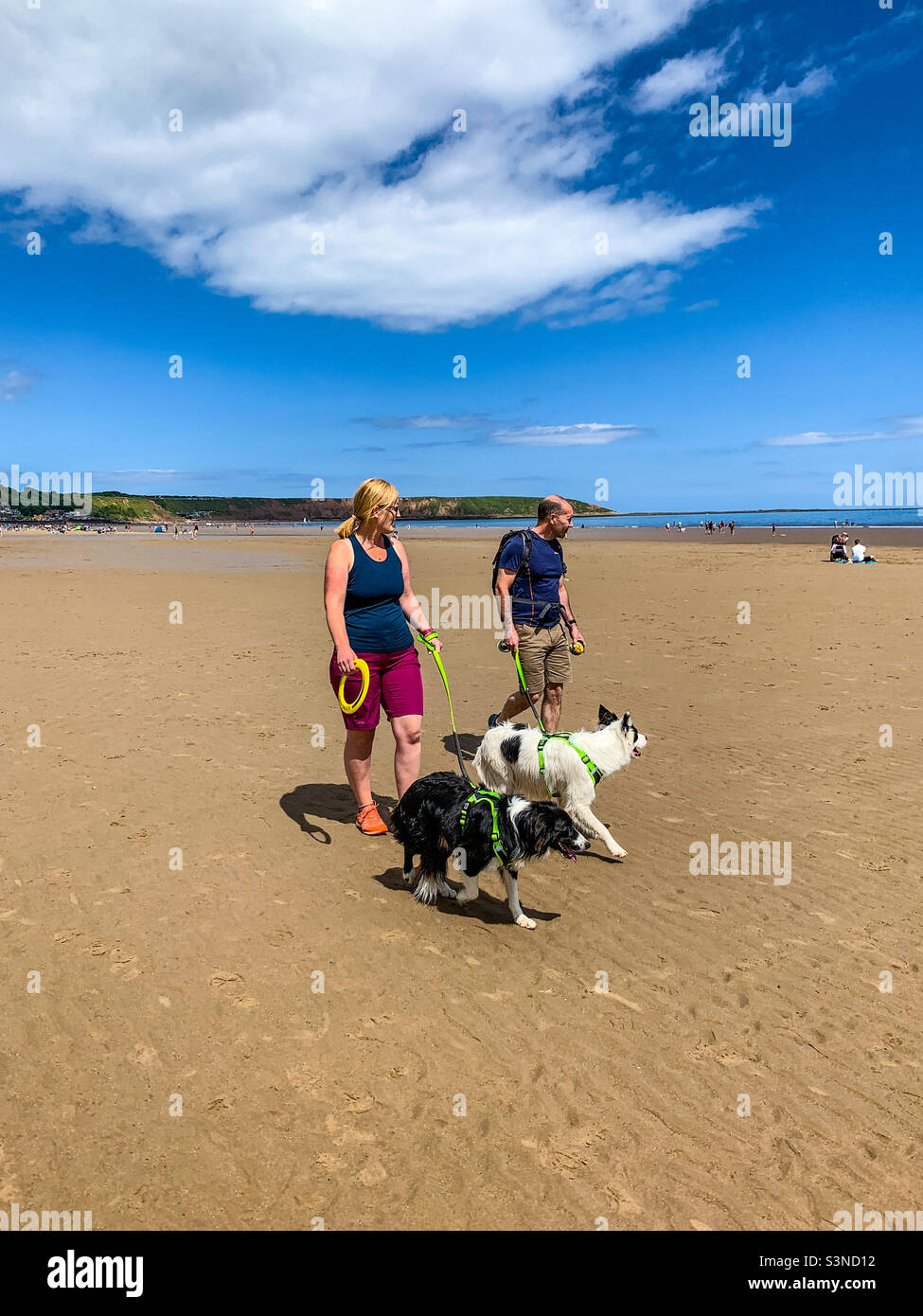Pärchen, die mit ihren schwarz-weißen Hunden am Strand von Filey Bay spazieren gehen Stockfoto