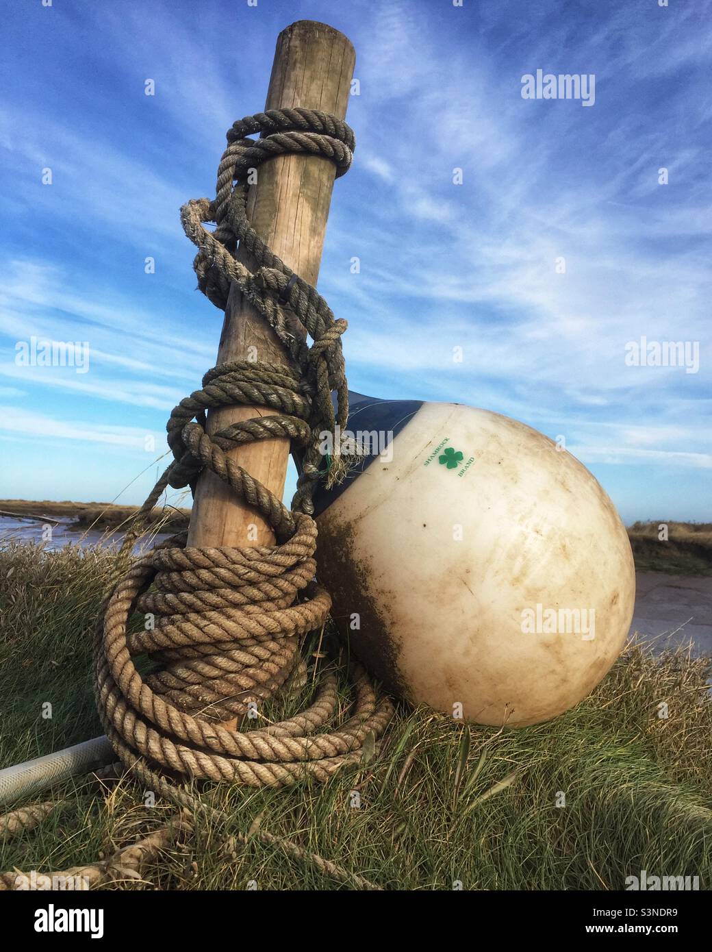 Eine Markierungsboje und ein Seil umwickelt einen Holzpfosten gegen einen blauen Himmel. Stockfoto