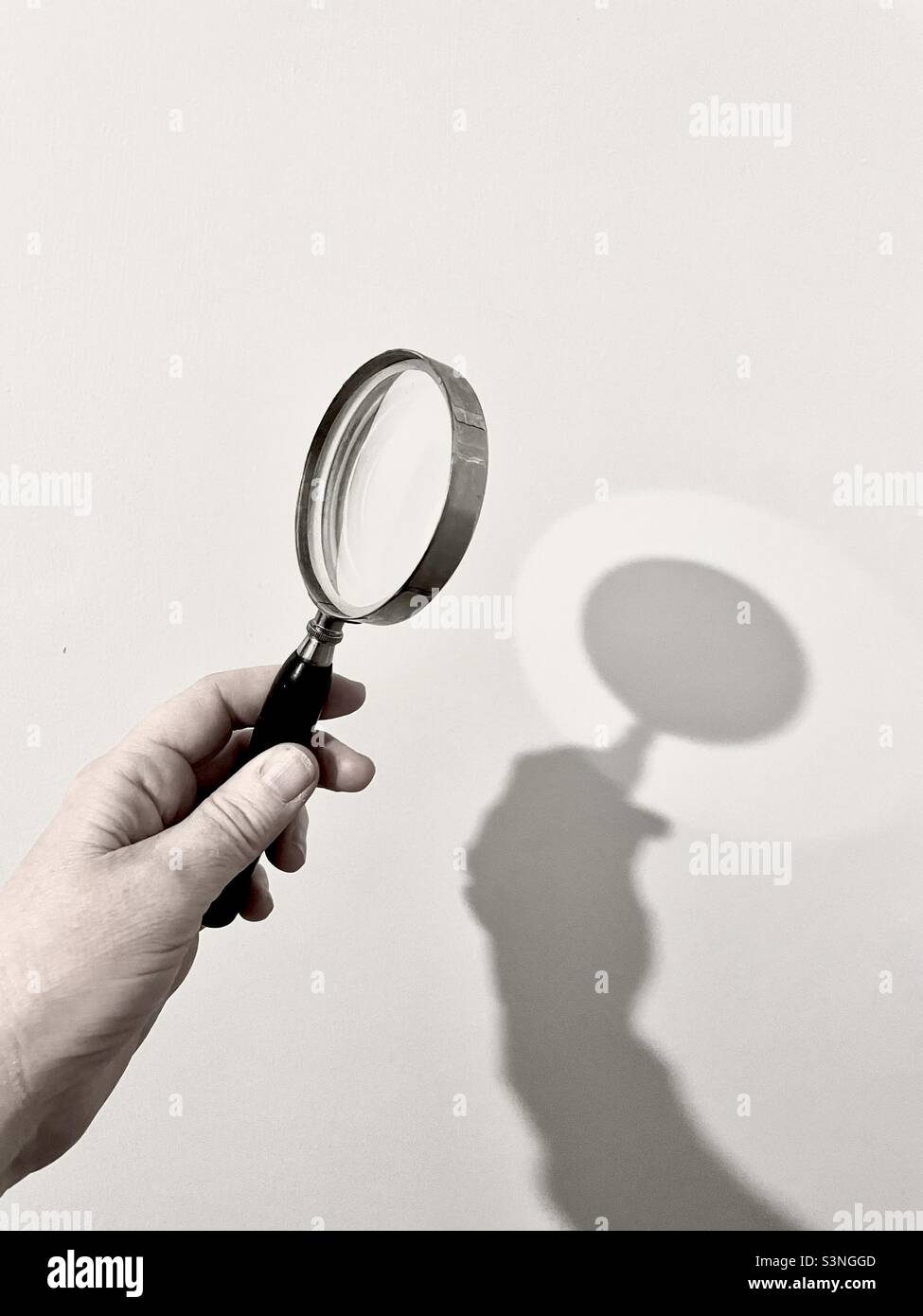 Hand hält eine Lupe und macht einen Schatten an der Wand. Stockfoto