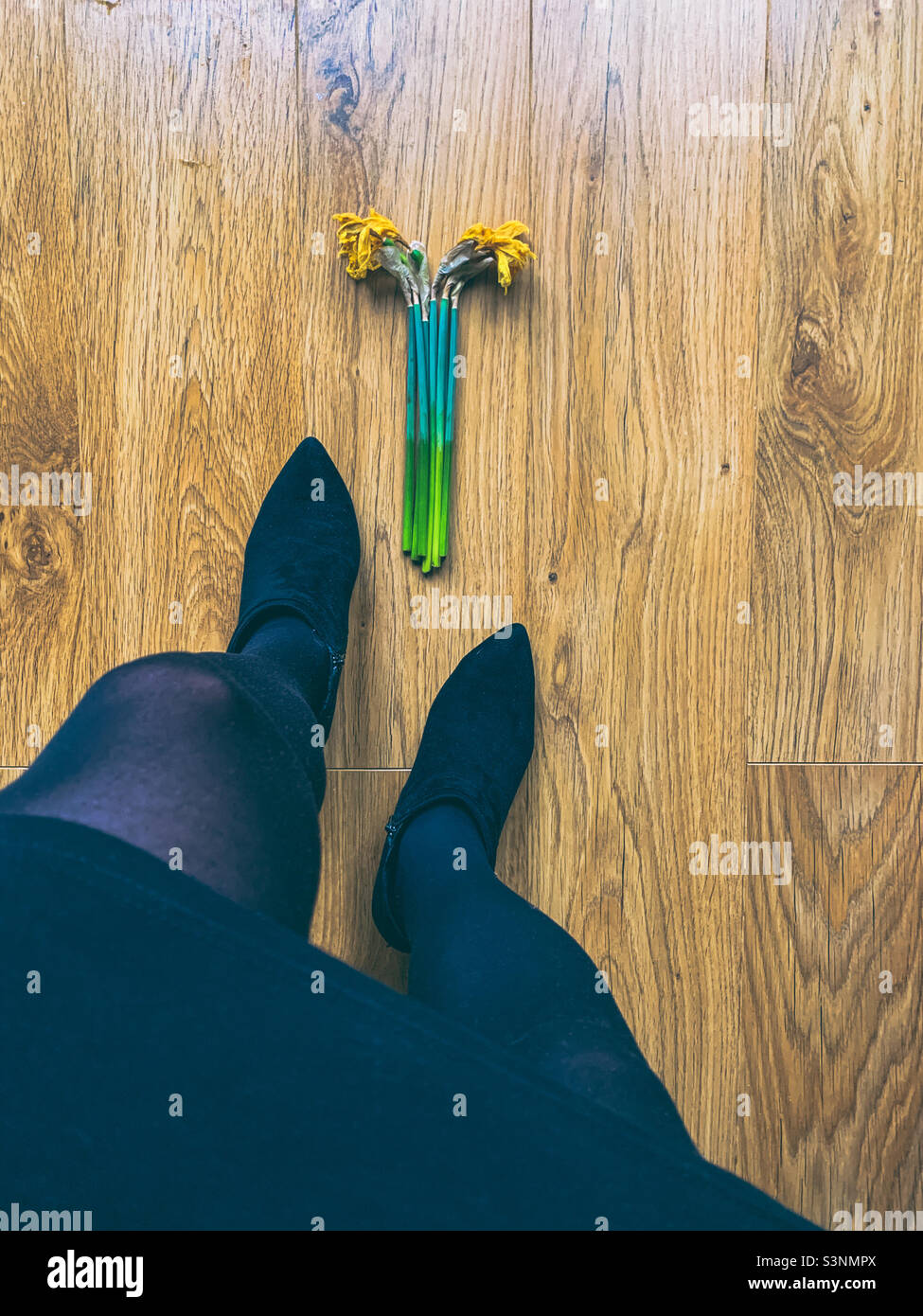 Tote Narzissen auf einem Holzboden, Draufsicht mit Frauenbeinen und Stiefeletten Stockfoto