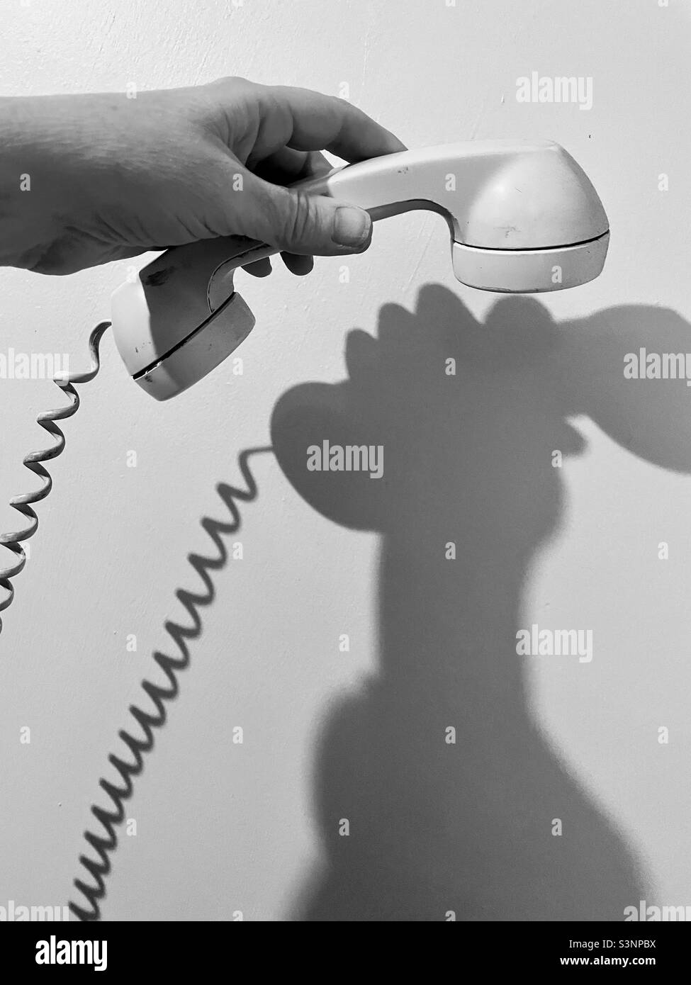 Hand hält einen altmodischen Telefonhörer mit Spiralkabel und Wandschatten. Stockfoto