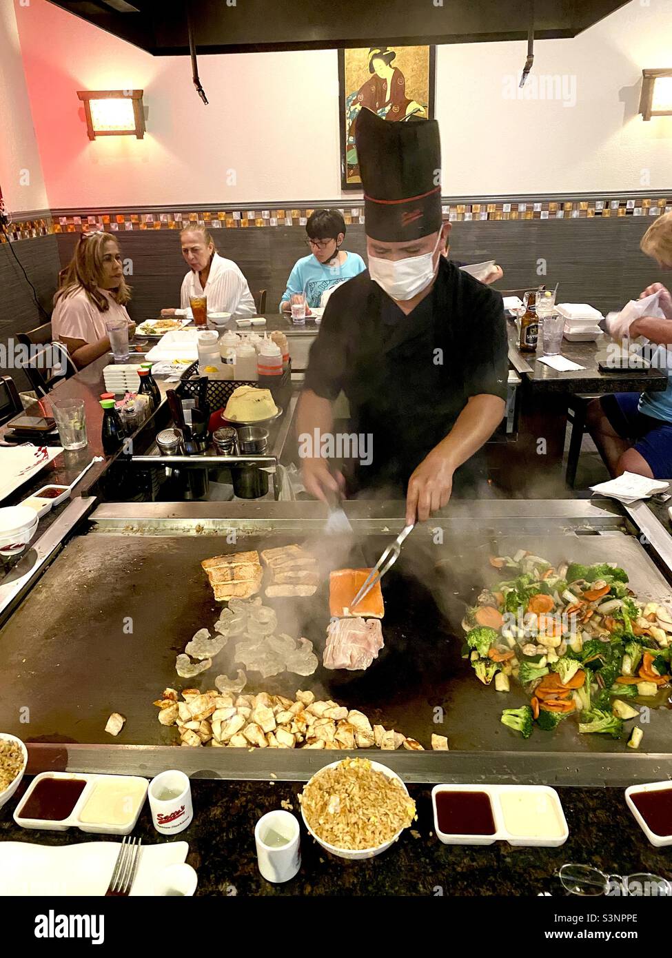 Der Hibachi Koch in einem japanischen Restaurant kocht Fisch Huhn und Fleisch auf einem heiBen Hibachi Ofentisch der von Gasten umgeben ist Stockfotografie Alamy