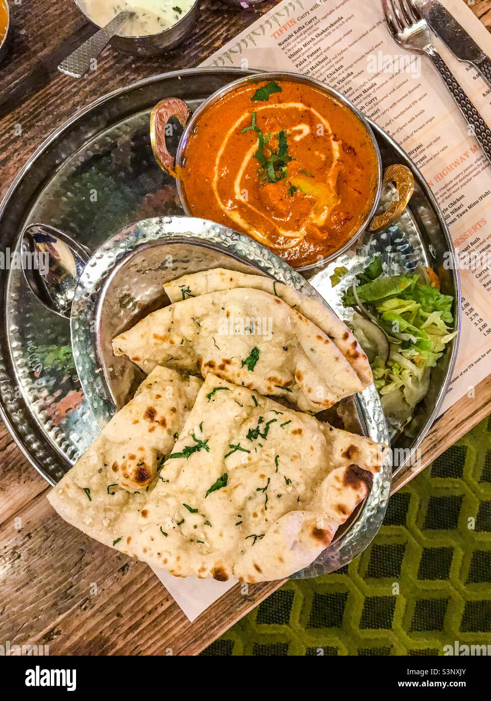 Hühnerplausch und Knoblauchnaan-Brot auf Silberplatte im indischen Restaurant - Smartphone-aufgenommenes Stockfoto