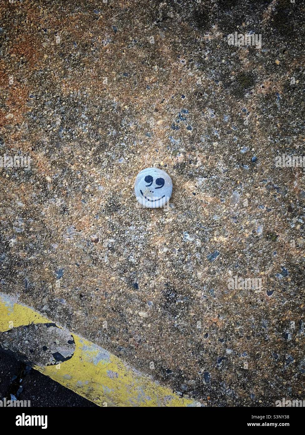 Ein fröhlich lächelnder Emoji auf einem Asphalt-Boden, der auf einem kleinen Stein gemalt ist Stockfoto