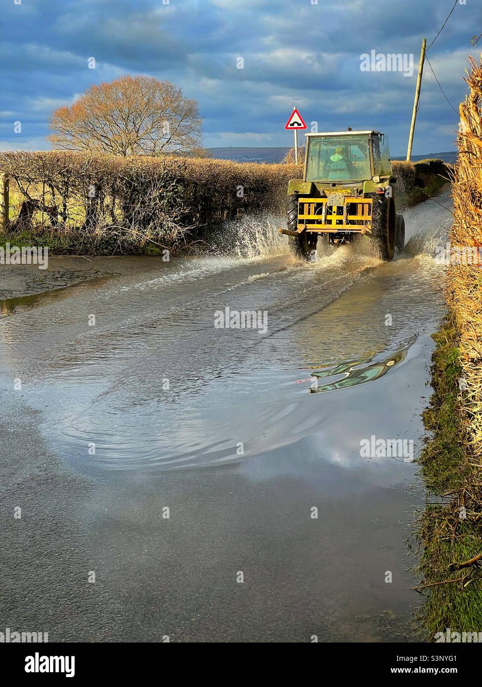 Traktor fährt durch eine überflutete Landstraße, South Wales, März. Stockfoto