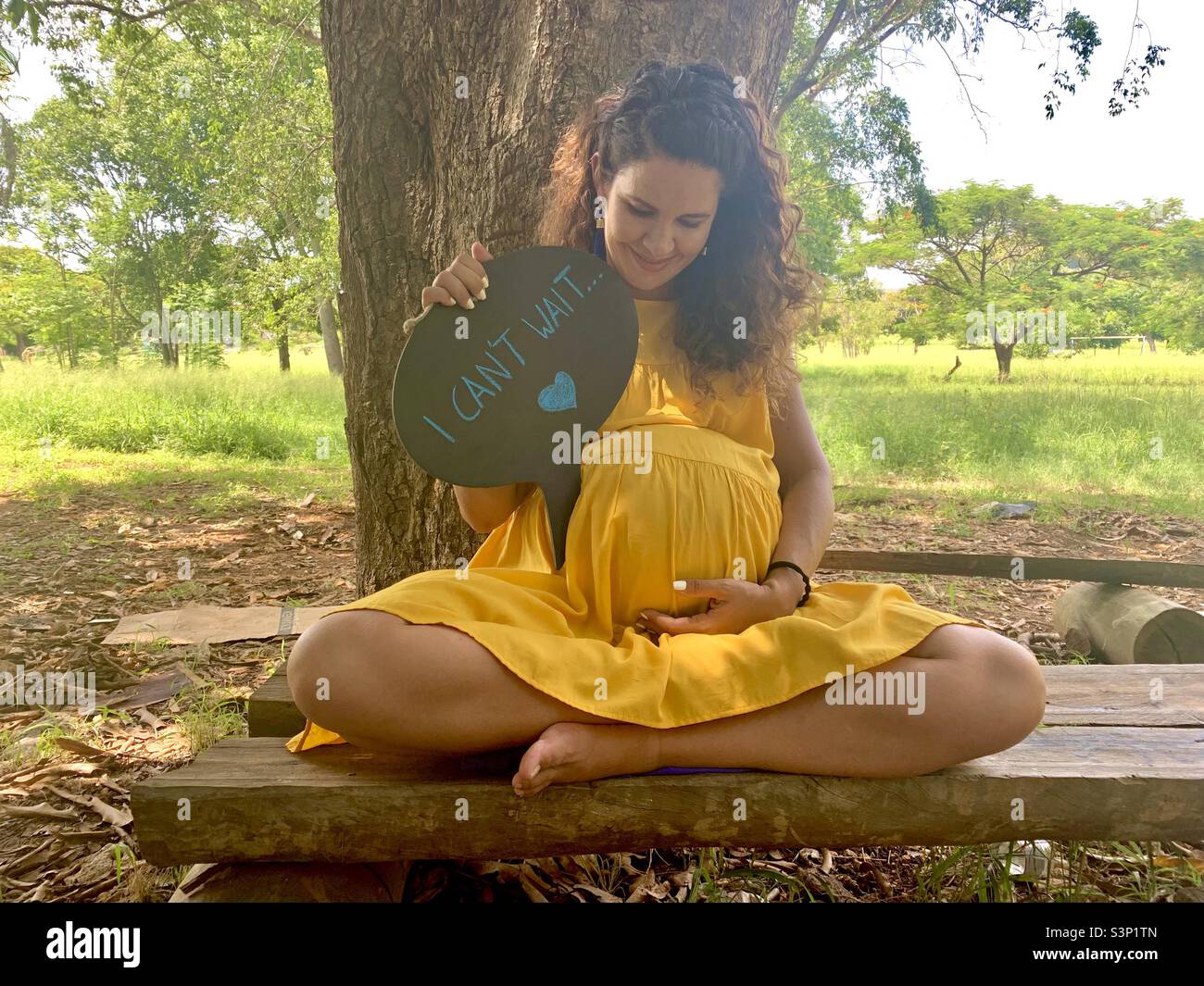 Eine schwangere Frau hält einen Text mit dem Titel „Ich kann nicht warten“, während sie glücklich auf ihren wachsenden Bauch blickt. Schwangerschaftsfotos. Havanna, Kuba, Karibik. Stockfoto