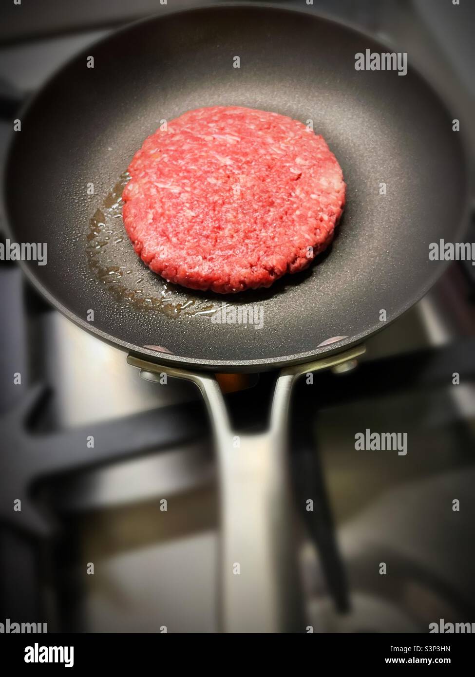 Nahaufnahme eines einzelnen Hamburger-Patties, der in einer kleinen Pfanne gebraten wird, 2022, USA - Smartphone-aufgenommenes Stockfoto