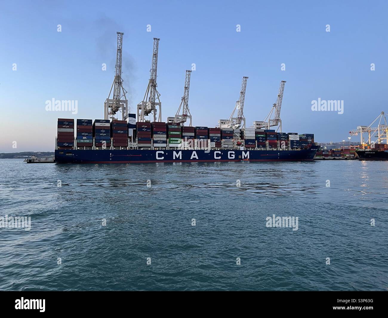 Großes Containerschiff CMA CGM voll beladen im Hafen von Koper, Slowenien, vertäut. Hinter dem Schiff befinden sich Portalkrane in vertikaler Position, die für den Be- und Entladebetrieb bereit sind. Stockfoto