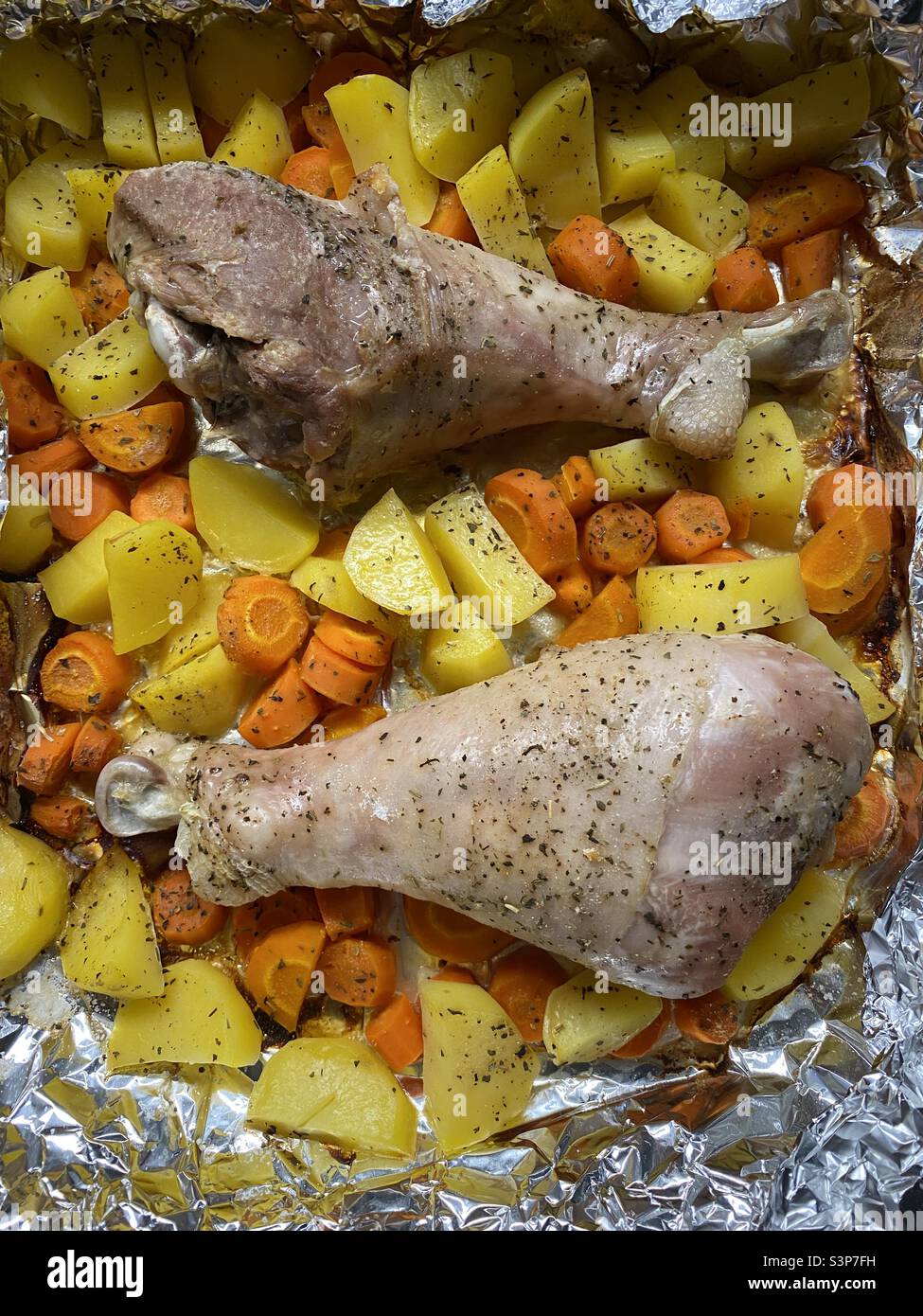 putenbeine mit Kartoffeln und Karotten in Gewürzen auf einem Backblech Stockfoto