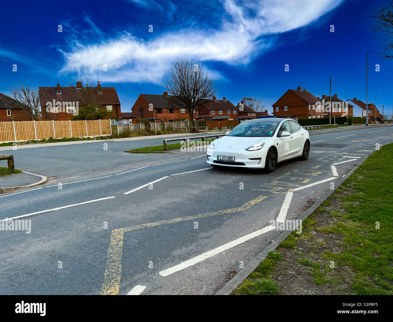White Tesla Model 3 Elektrofahrzeug fährt in der Stadt - Smartphone-aufgenommenes Stockfoto