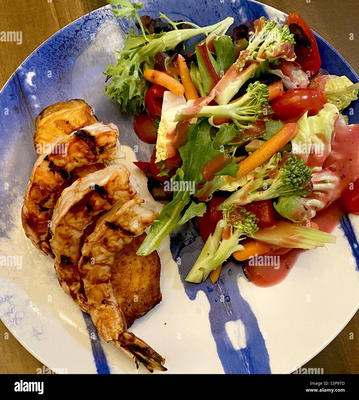 Nahaufnahme eines Tellers mit gegrillten Garnelen über gegrilltem Lachs mit Gemüse und Salat. Stockfoto