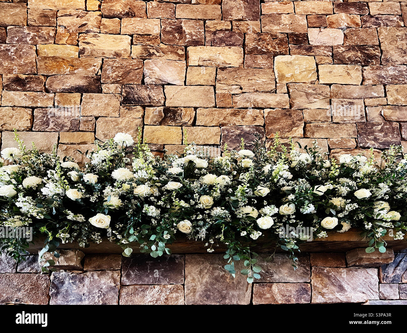 Hochzeitsblumen auf dem Mantel eines gestapelten Steinkamins im Innenbereich. Stockfoto