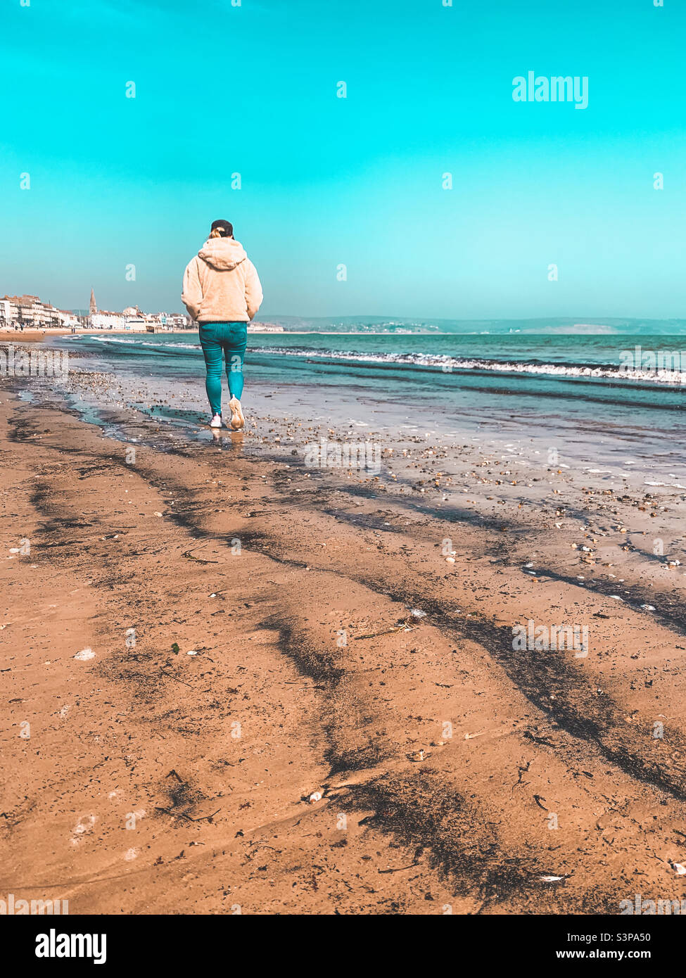 Frau, die alleine am Strand in Weymouth, Großbritannien, läuft (Mar22) Stockfoto