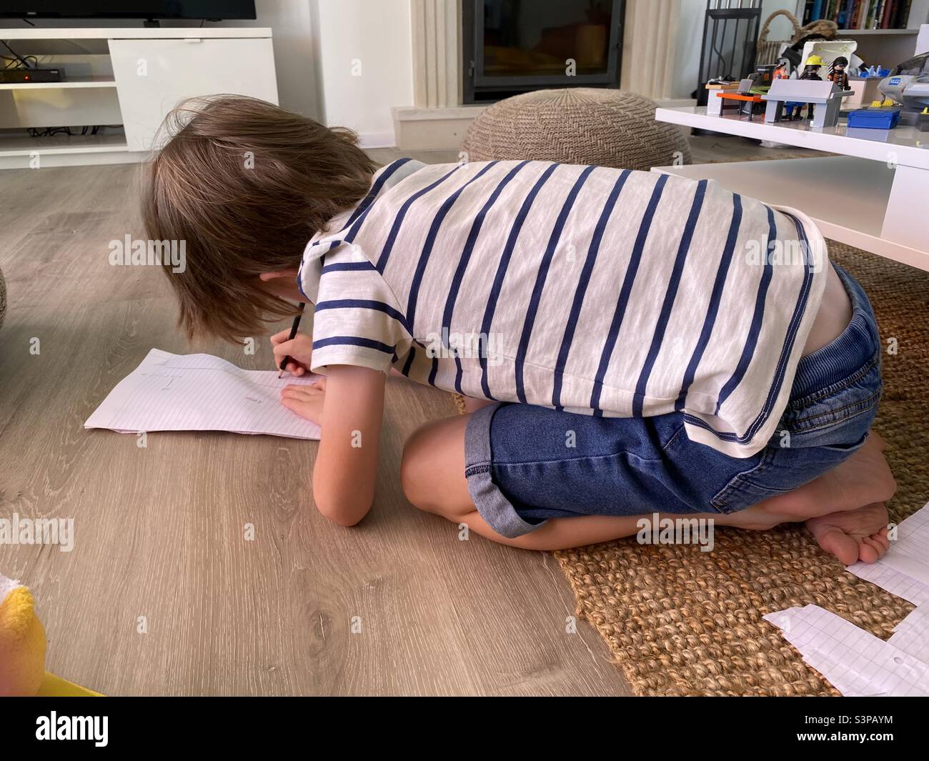 Kleiner Junge kniet auf dem Boden und zeichnet auf weißem Papier Stockfoto