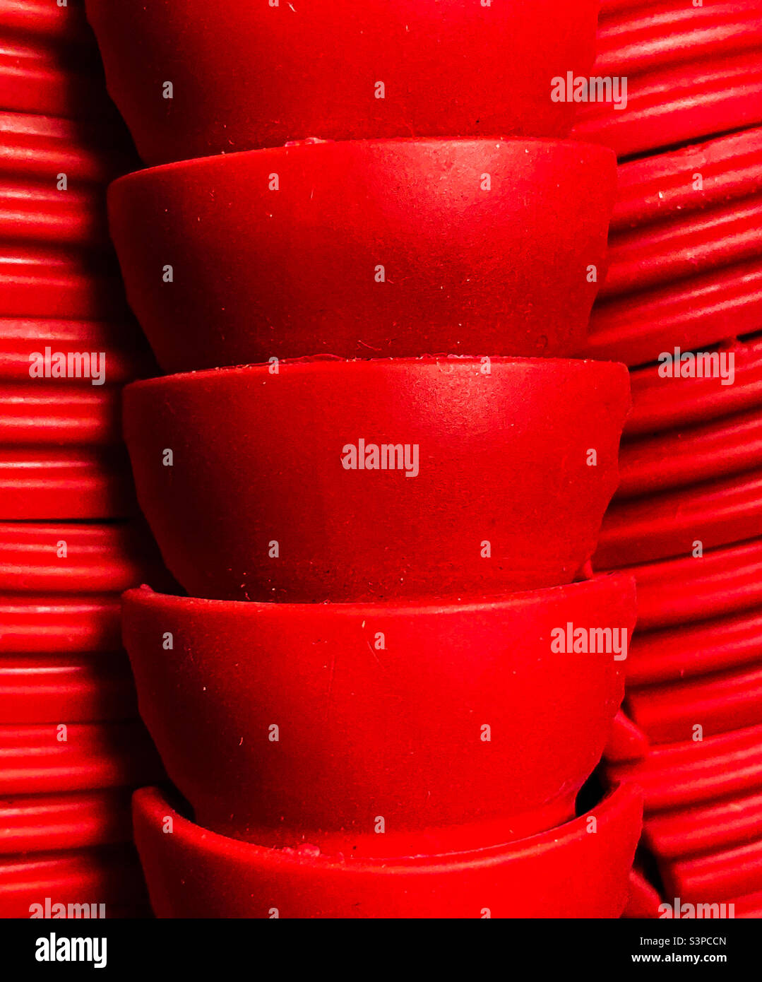 Abstraktes, ganz rotes Bild, bestehend aus einem Stapel von tassenförmigen Objekten in der Mitte, mit Reihen paralleler Linien hinter ihnen auf beiden Seiten (Nahaufnahme von gummierten Stativbeinen). - Smartphone-aufgenommenes Stockfoto