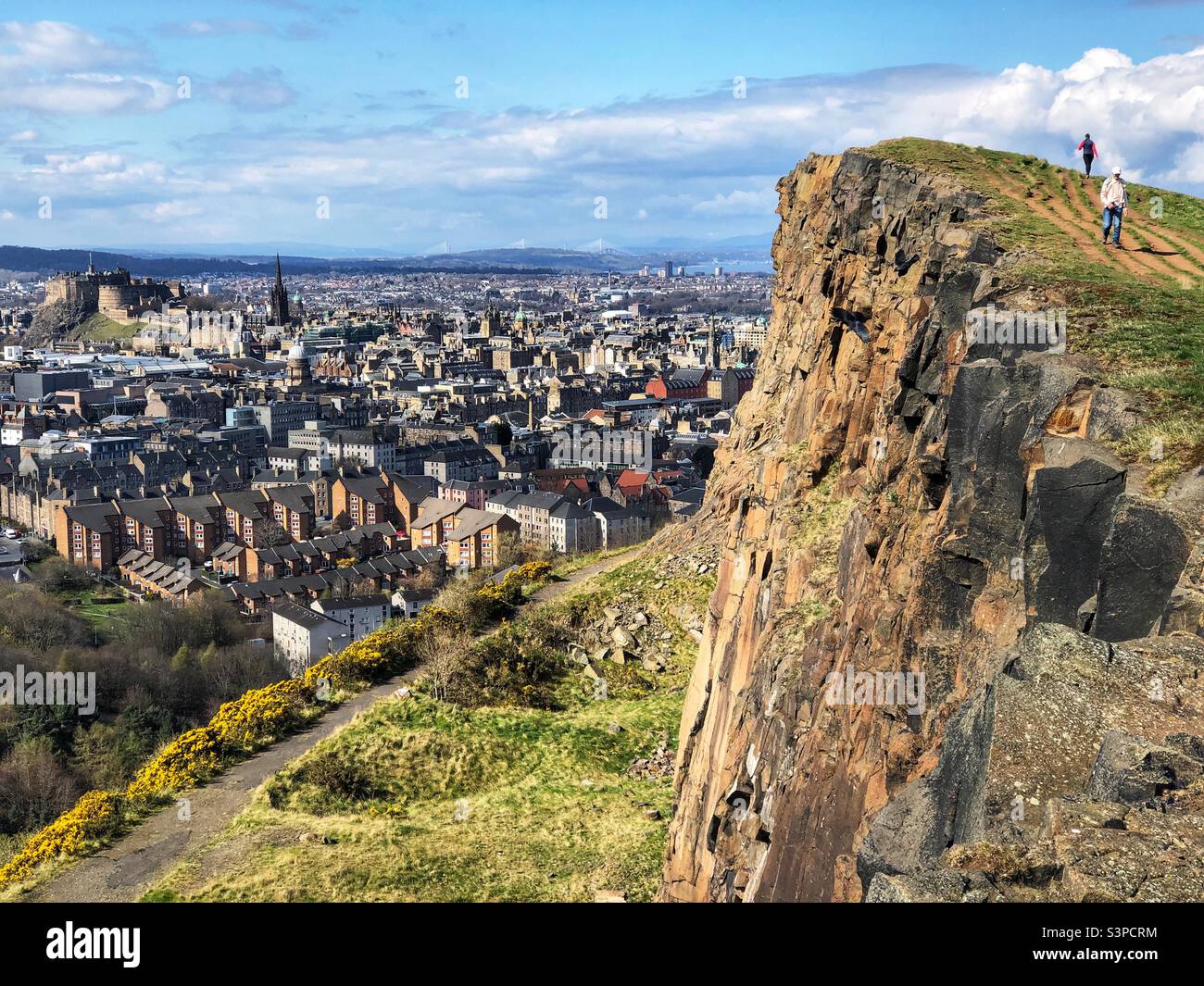 Menschen auf Salisbury Crags mit Blick auf die Burg von Edinburgh und die Dächer der Stadt, Holyrood Park, Edinburgh Schottland - Smartphone-aufgenommenes Stockfoto
