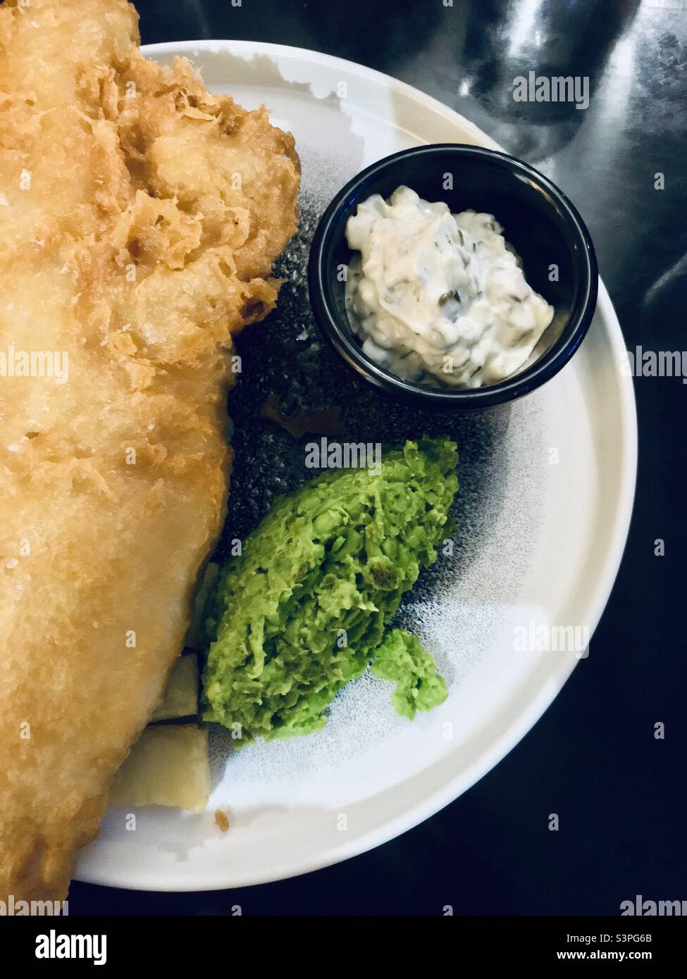 Fish and Chip Supper – zerbrochener Kabeljau und klobige Chips mit zerdrückten Gartenerbsen und Tartaresauce Stockfoto