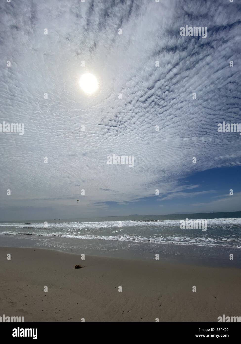 Die Sonne scheint durch die Wolken, während kleine Wellen am Pazifik am Ventura Beach, Kalifornien, brechen. Gleitschirm sichtbar und Inseln in der Ferne Stockfoto
