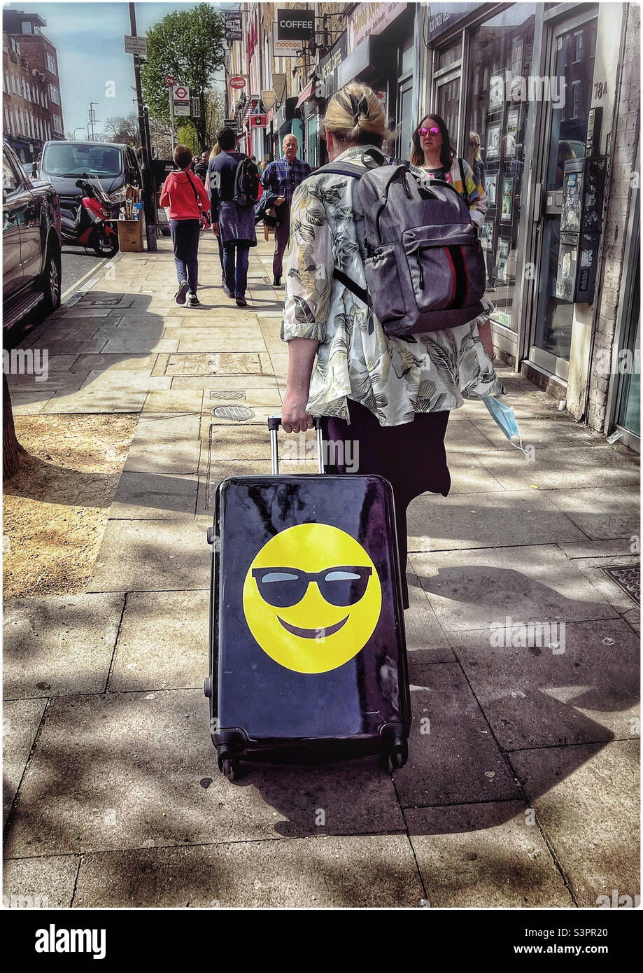 Eine Frau zieht einen mit einem Smiley-Emoji geprägten Koffer entlang einer Londoner Straße Stockfoto