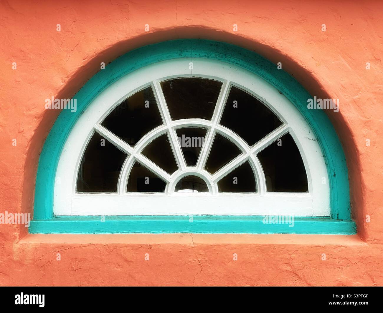 Halbkreisförmiges Fenster in einer pfirsichfarbenen Wand in Portmeirion, Gwynedd, Nordwales. Stockfoto