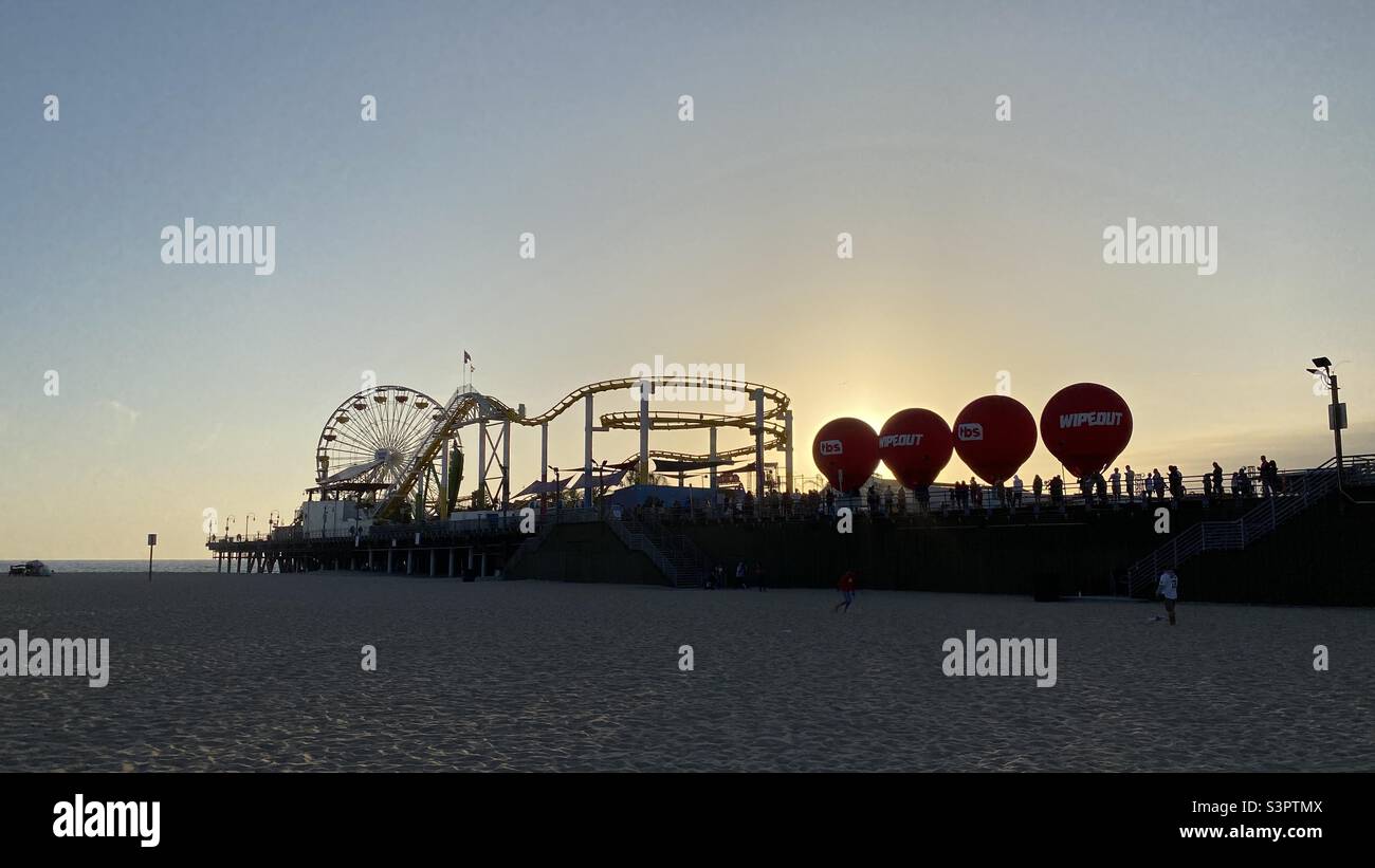 SANTA MONICA, CA, APR 2021: Sonnenuntergang hinter roten Ballons am Pier, Silhouetten-Achterbahn und Riesenrad Stockfoto