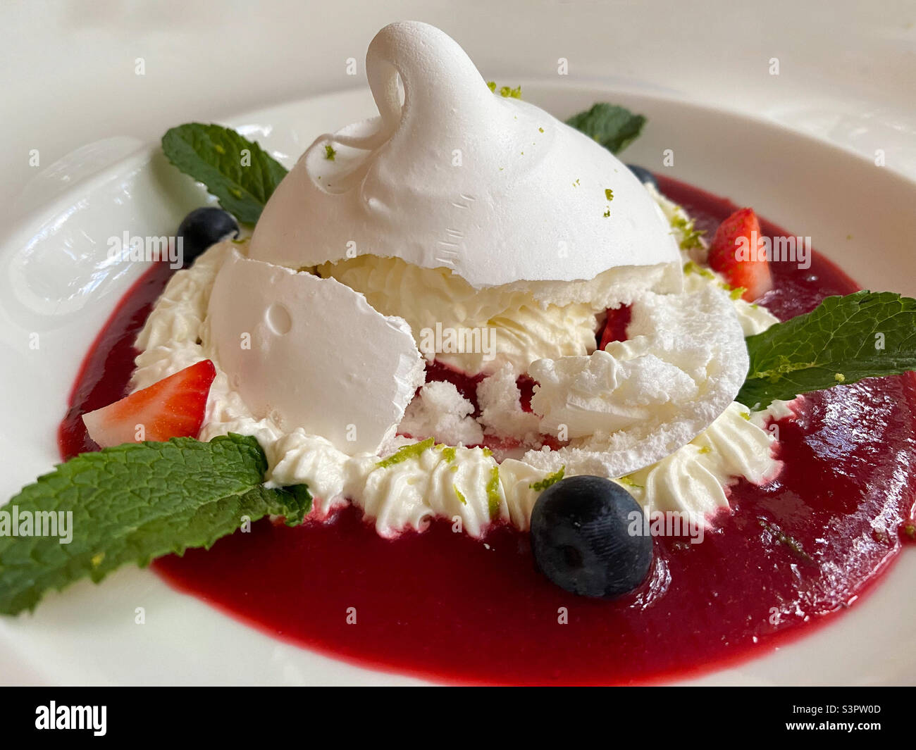 Köstliches Pavlova Dessert auf einem weißen Teller aus der Nähe. Pavlova Dessert ist eine luftige weiche Wolke und eine erstaunliche Geschmackskombination aus Beeren, Buttercreme und Proteinteig Stockfoto