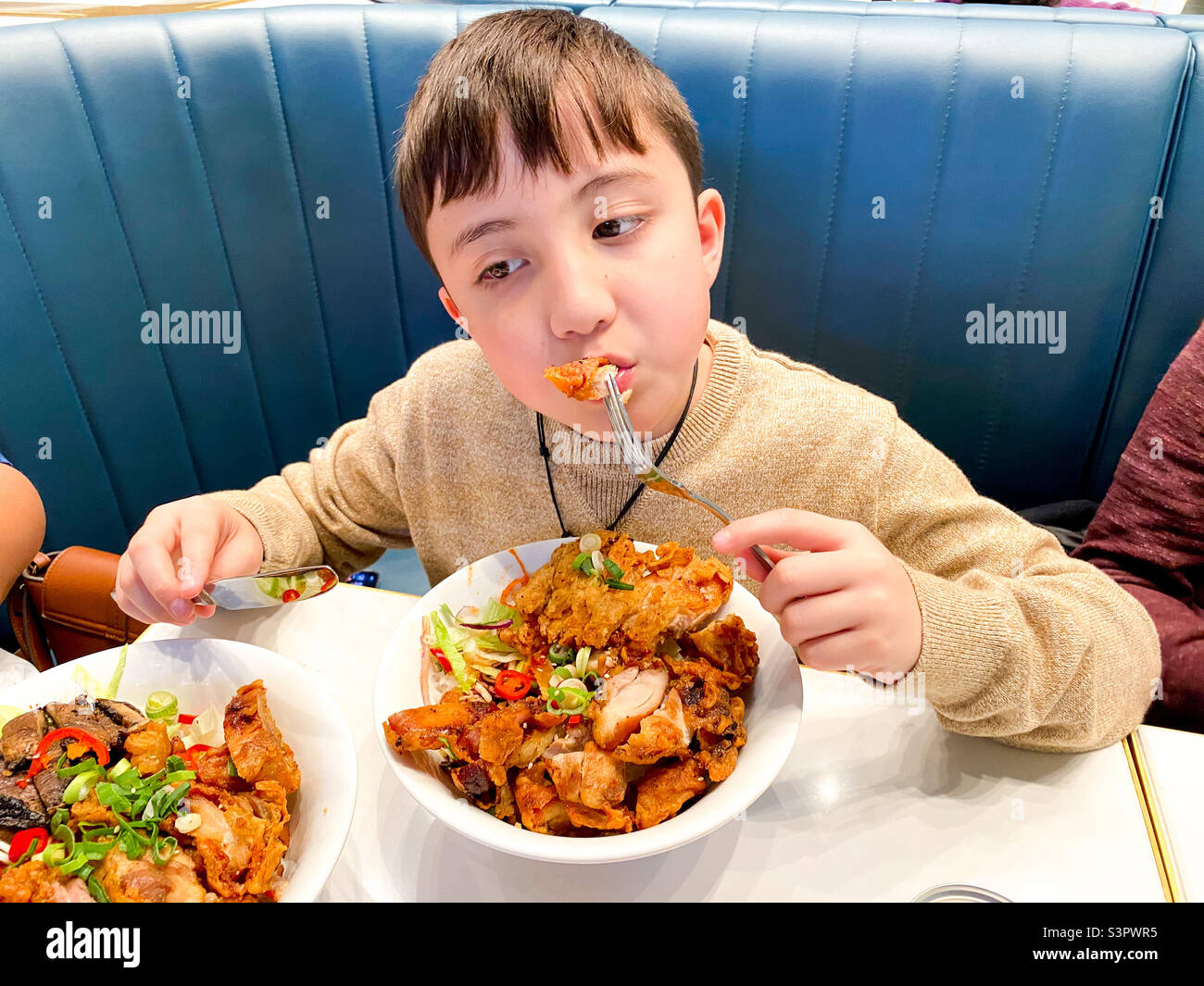Ein Junge, der eine Schüssel mit Essen in einem Lebensmittelbereich isst. - Smartphone-aufgenommenes Stockfoto