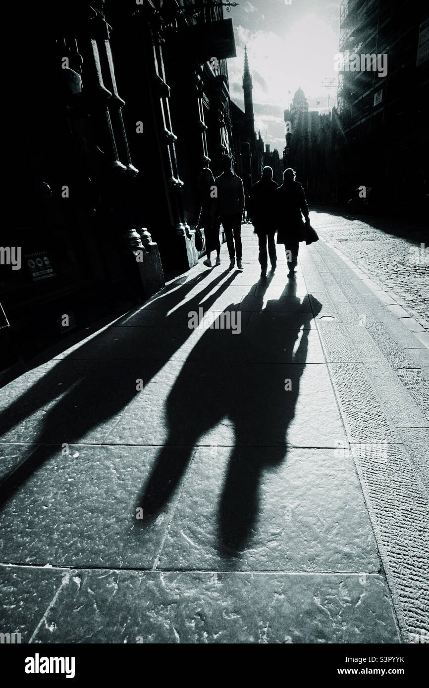 Menschen, die entlang der Royal Mile in Edinburgh spazieren, werden von der späten Nachmittagssonne beleuchtet und werfen lange Schatten Stockfoto