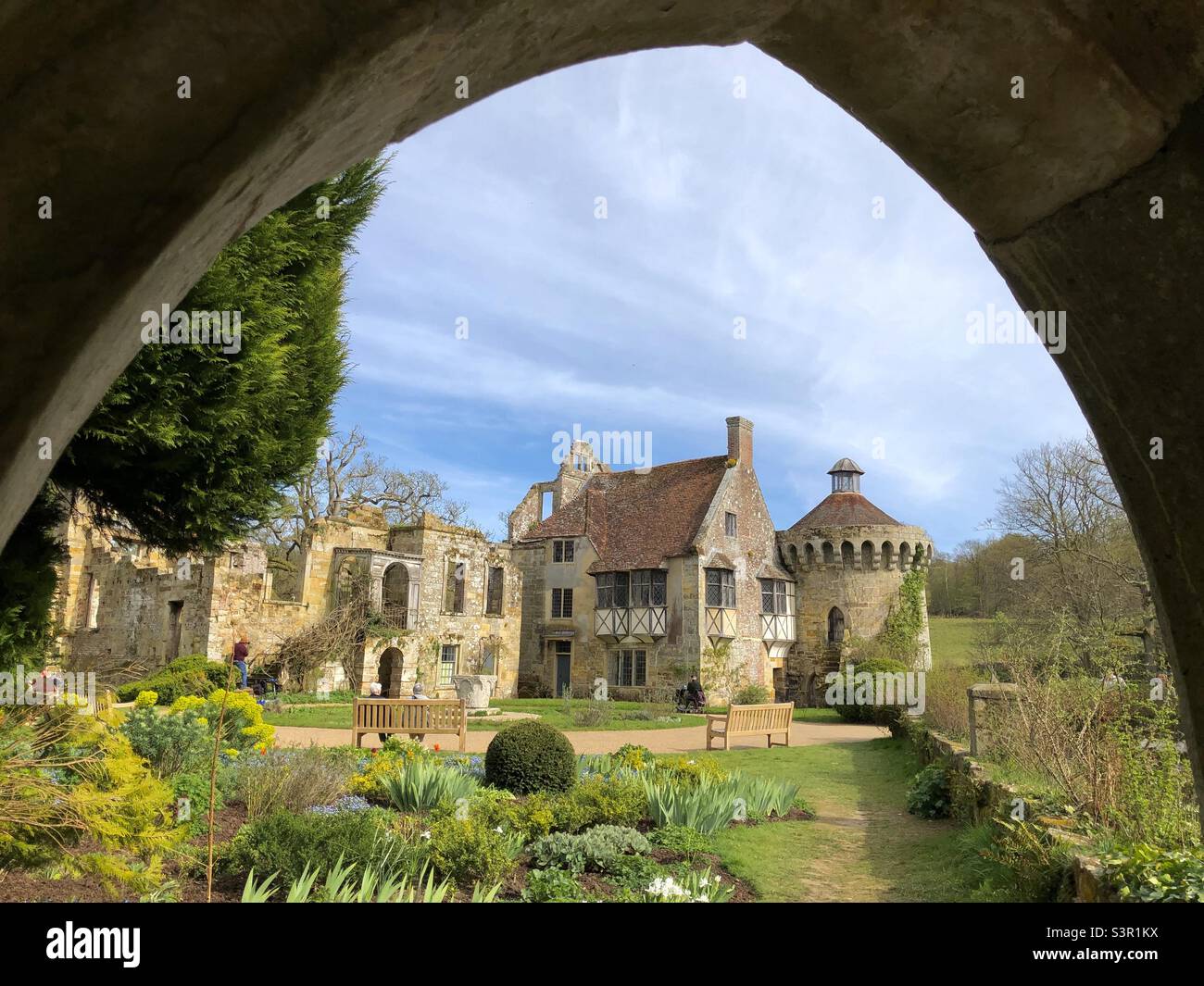 Das Scotney Castle ist von einem alten Steinbogen mit blauem Himmel und Pastellfarben durchleuchtet und eingerahmt. - Smartphone-aufgenommenes Stockfoto