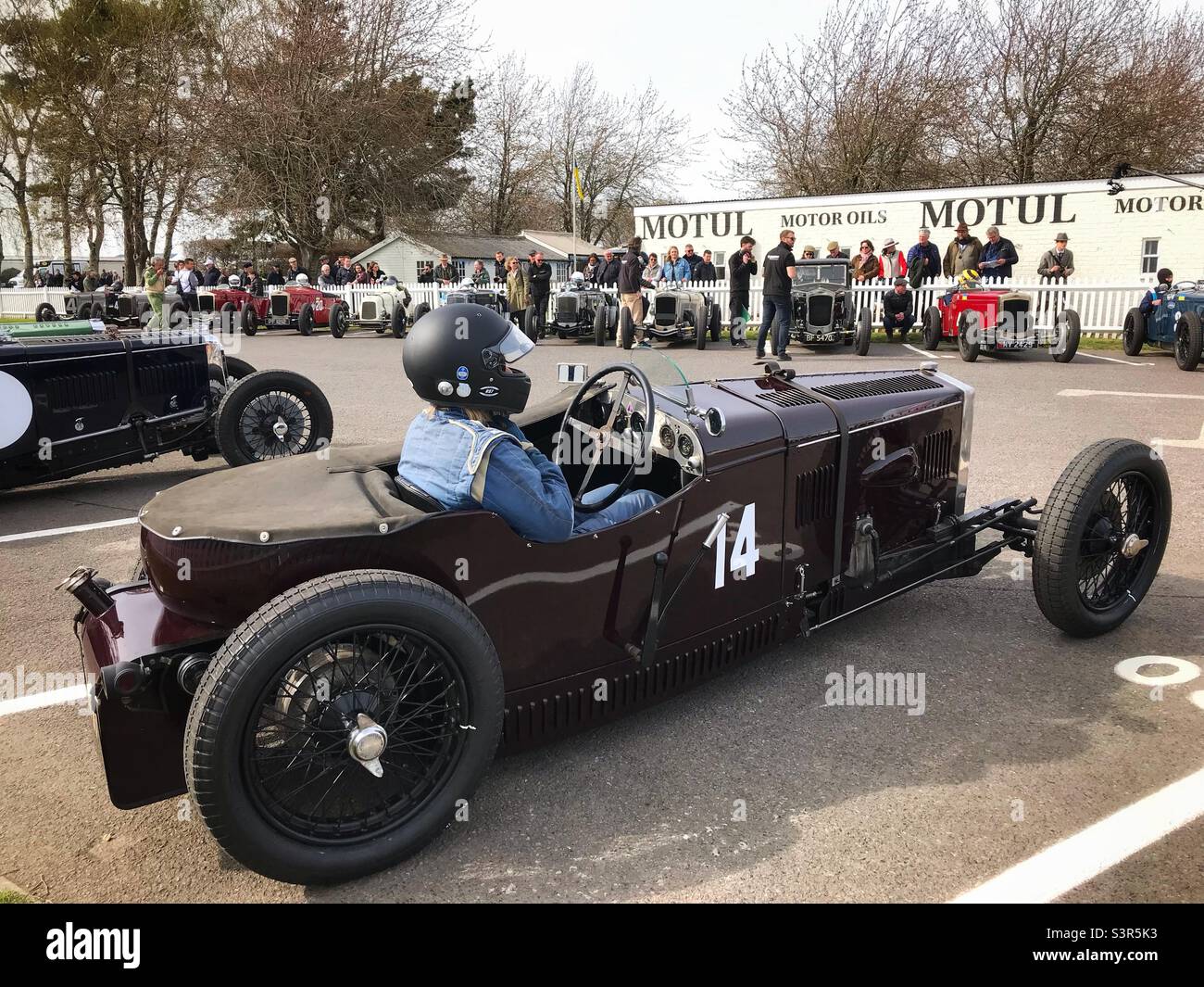 Eine Frau, die in ihrem Frazer Nash-Rennwagen im Versammlungsbereich von Goodwood für die Mitgliederversammlung 79. sitzt. - Smartphone-aufgenommenes Stockfoto
