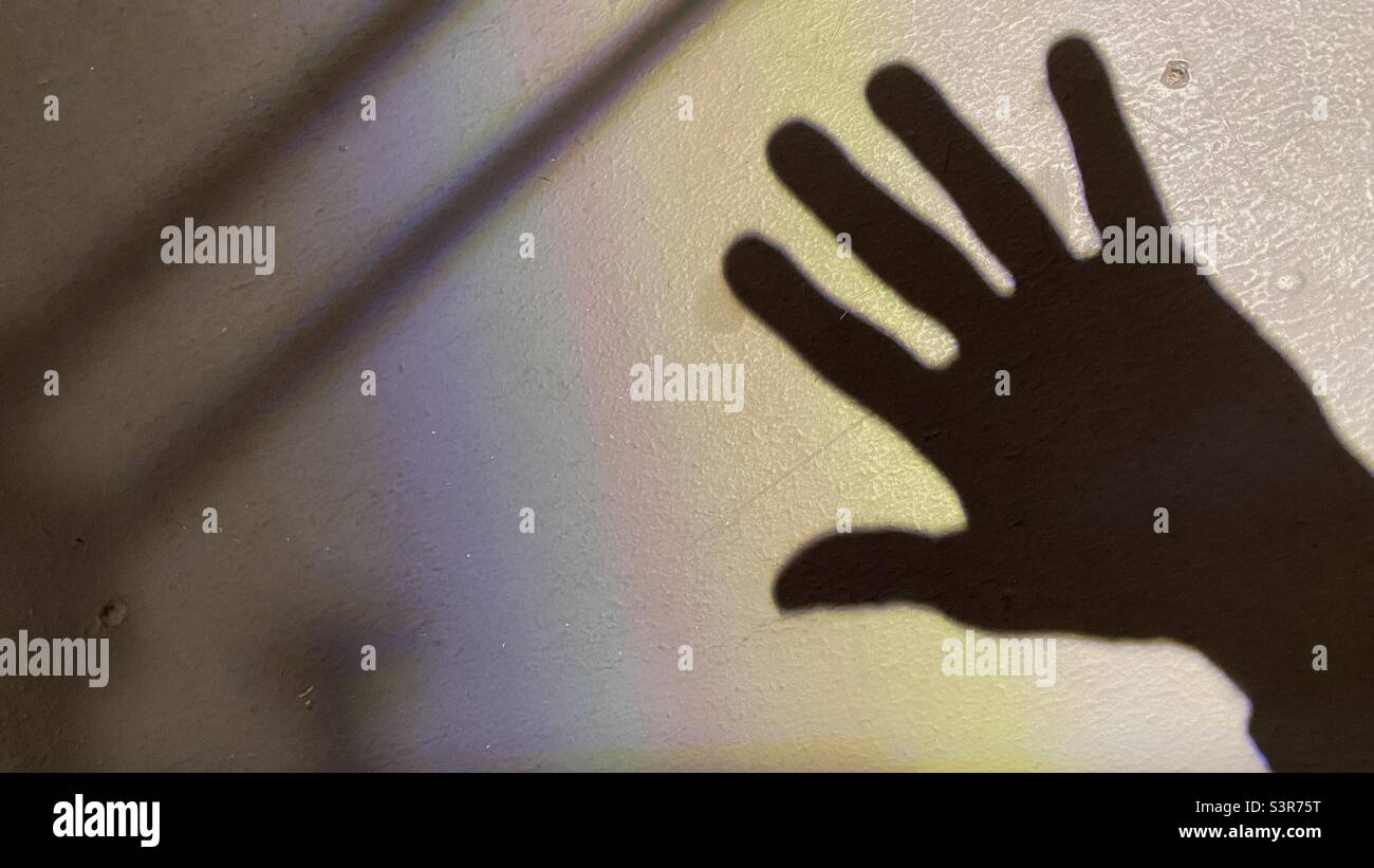 Schatten einer Hand auf einer weißen strukturierten Oberfläche, mit farbigem Beugungsmuster von einer Lichtquelle mit Linse - Smartphone-aufgenommenes Stockfoto