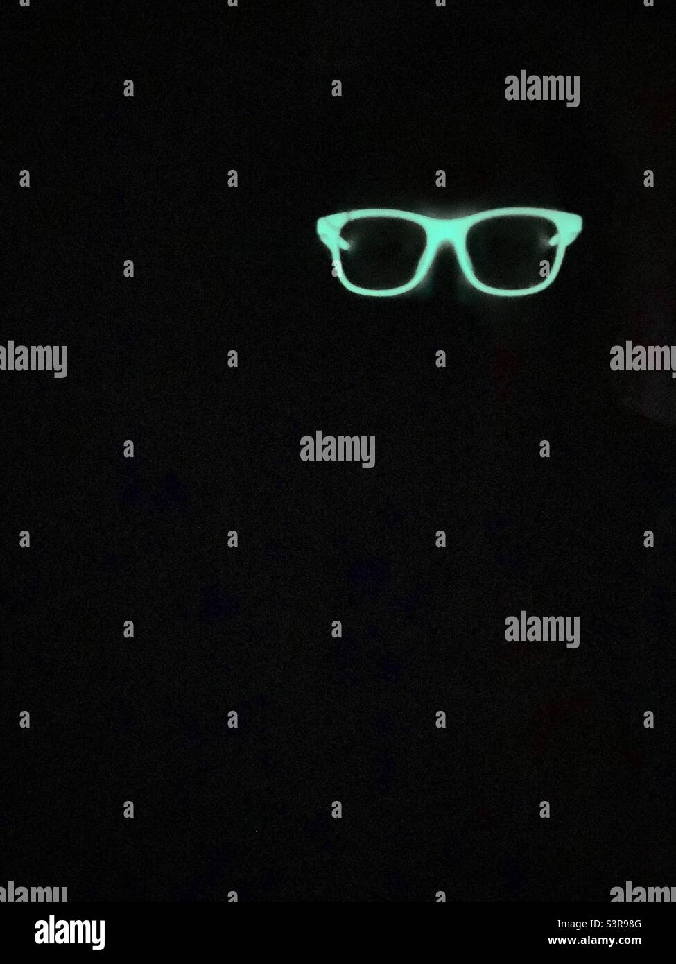 Im Dunkeln leuchtende Brillen scheinen in der Dunkelheit zu schweben. Stockfoto