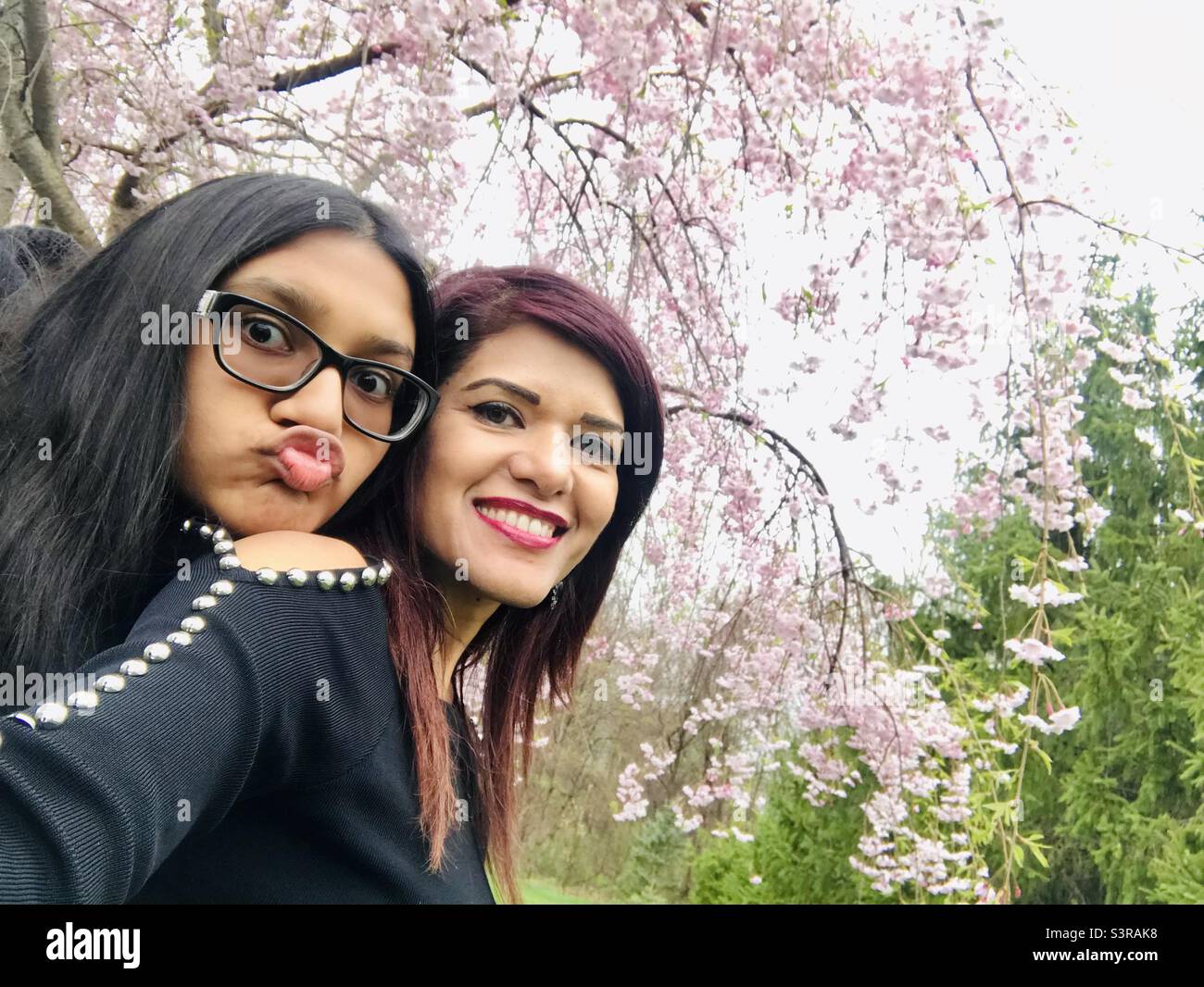 Eine Mutter und Tochter genießen den Frühlingstag im Freien und machen gemeinsam ein Selfie, während die Tochter spielerisch einen Pudel macht Stockfoto