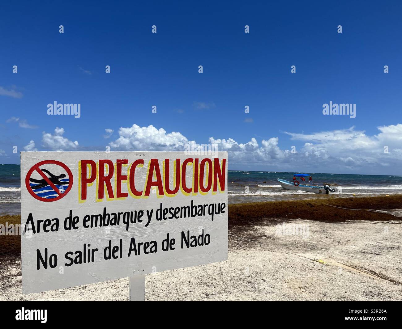 Vorsicht - Warnschild mit der Aufschrift - Precaucion Area de Embarque y Desembarque - mit zwei kleinen Booten in der Nähe am Tulum Beach, Mexiko - Smartphone-aufgenommenes Stockfoto