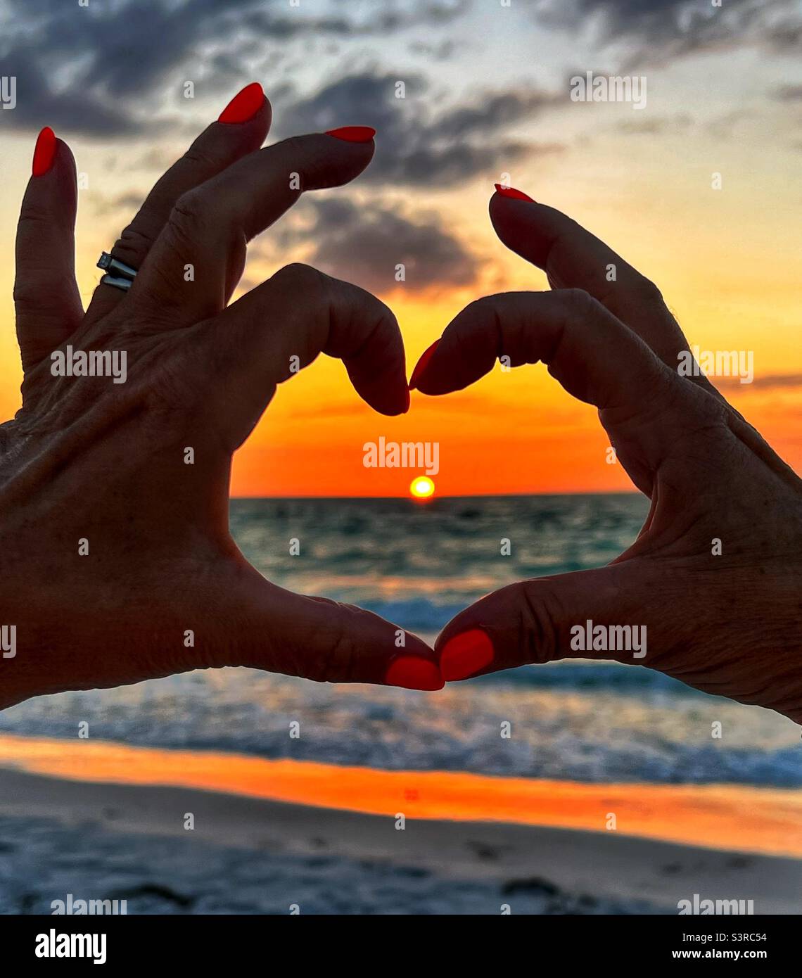 Sonnenuntergang durch Hände geformt wie ein Herz am Bean Point Beach auf Anna Maria Island in Florida USA Stockfoto