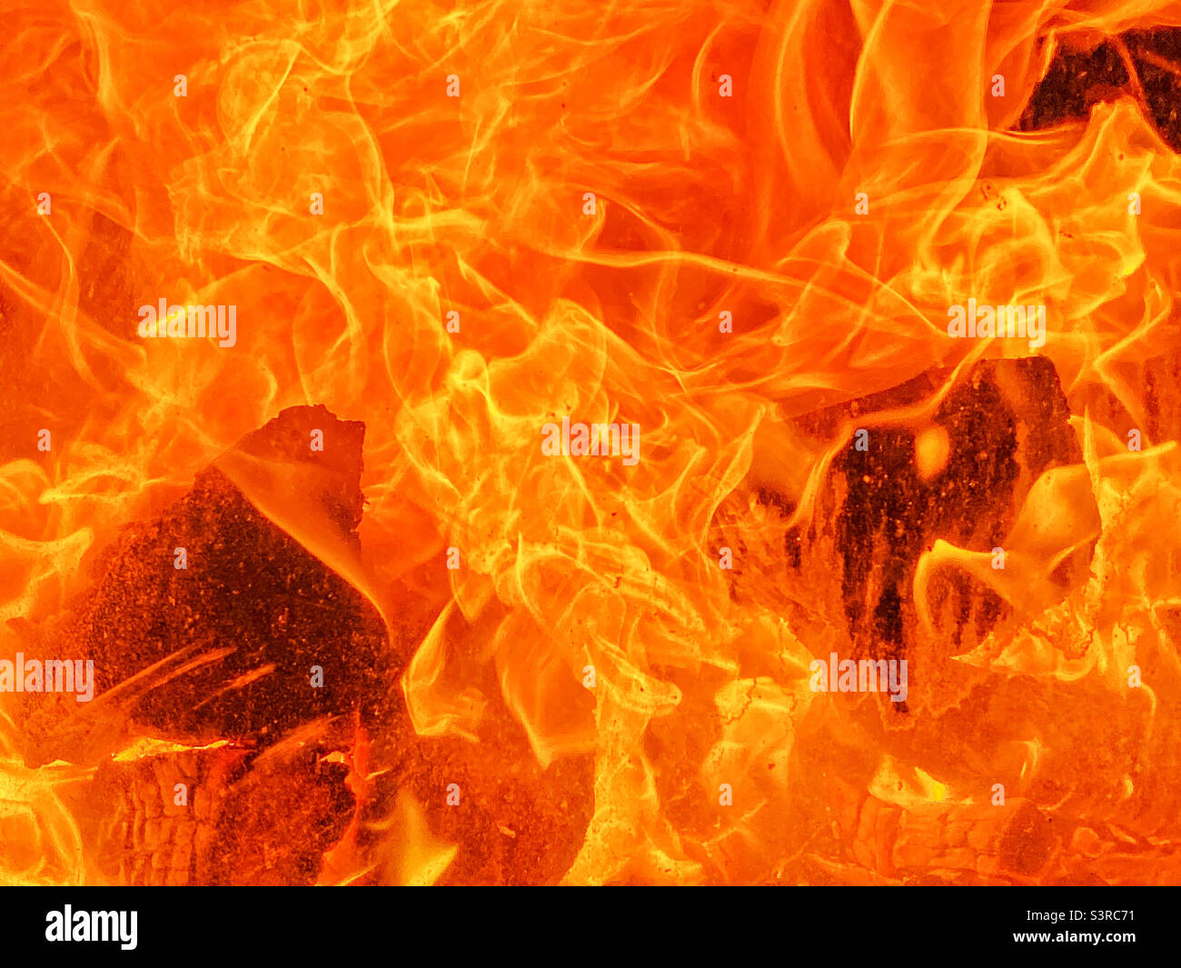 Zwei Holzstämme sind vollständig in die Flammen eines tobenden Feuers verschlungen. Es ist heiß und Zerstörung ist unvermeidlich. Viele gelbe und orangefarbene Flammen. Foto ©️ COLIN HOSKINS. - Smartphone-aufgenommenes Stockfoto