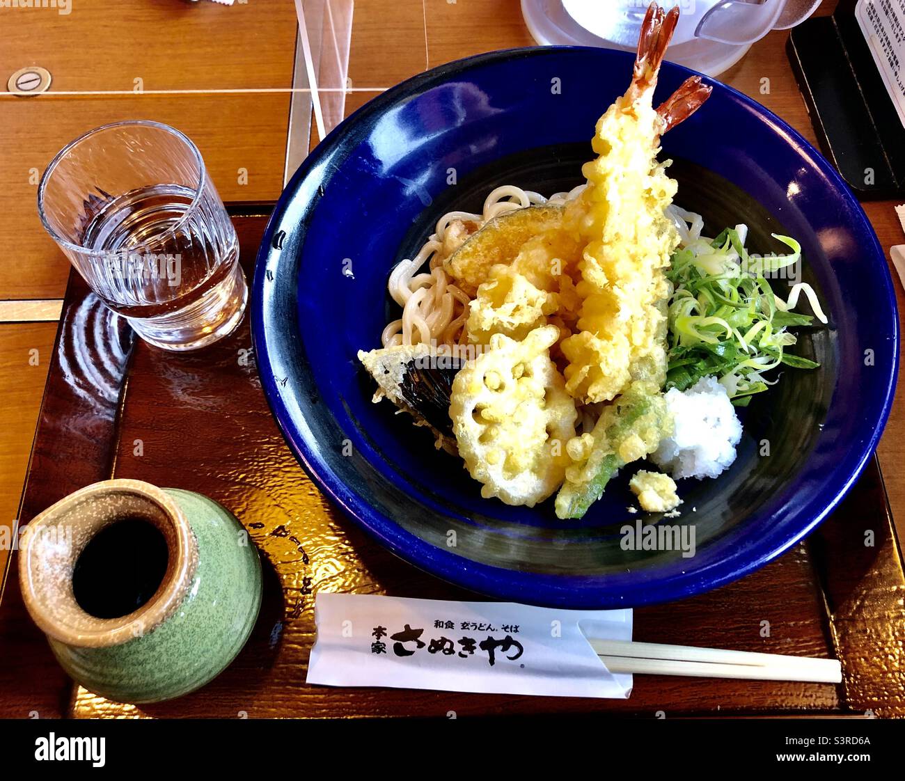Japanische udon-Nudeln mit Shrimp Tempura und Gemüse auf einer blauen Schüssel, traditionelles japanisches Mittagessen - Smartphone-aufgenommenes Stockfoto