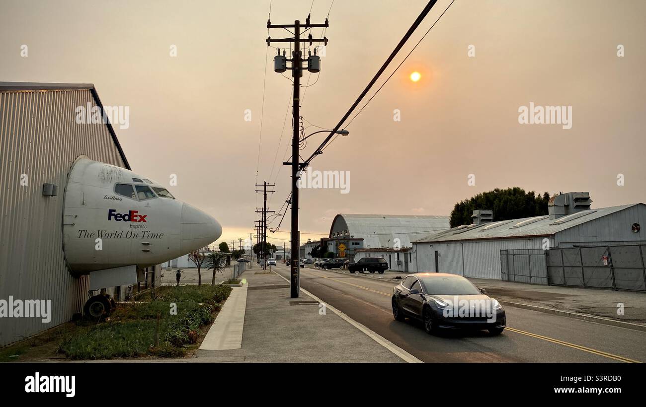 LOS ANGELES, CA, SEP 2021: Seitenansicht, Cockpit von Düsenflugzeugen, die von FedEx verwendet werden, scheint durch Hangarmauer zu Straße mit vorbeifahrenden Wagen im Museum of Flying, Santa Monica zu kommen. Trübe Sonne sichtbar Stockfoto