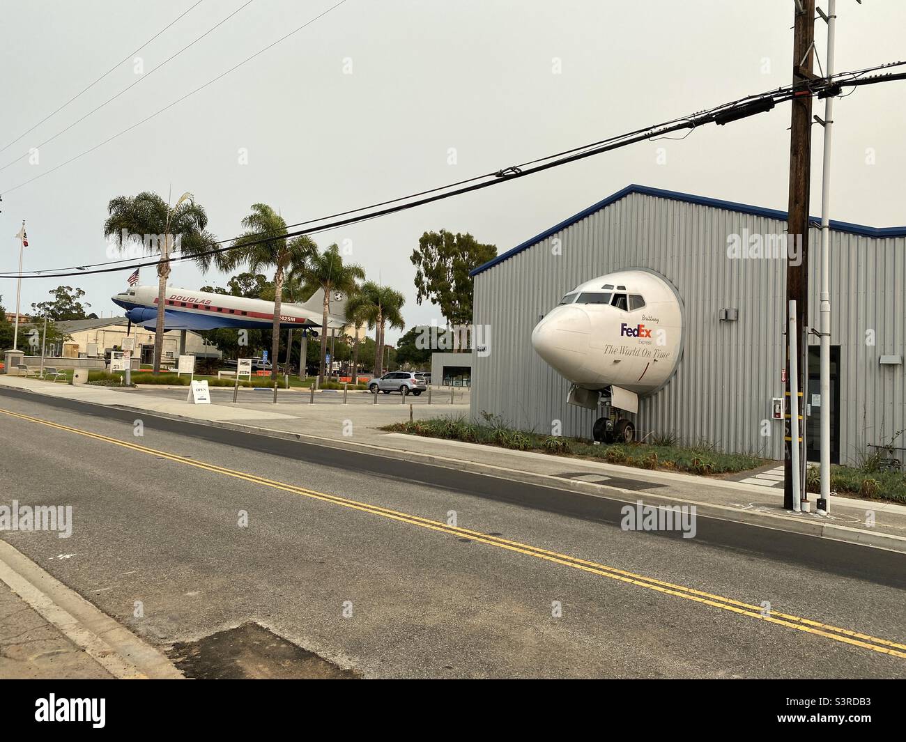 LOS ANGELES, CA, SEP 2021: Seitenansicht, Cockpit von Düsenflugzeugen, die von FedEx verwendet werden, scheint durch Hangarmauer auf Straße zu kommen, mit Douglas DC-3 hinter dem Museum of Flying, Santa Monica - Smartphone-aufgenommenes Stockfoto